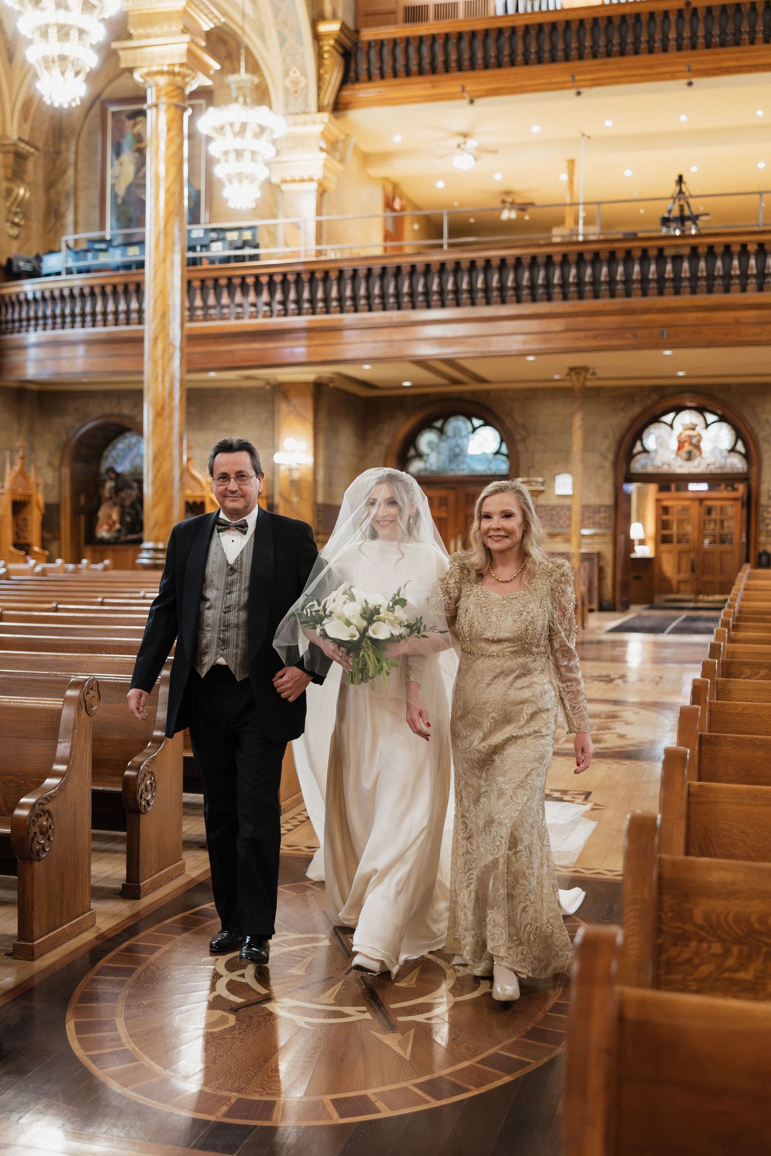 Wedding party members pose in an elegant church sanctuary with ornate woodwork and glowing chandeliers.