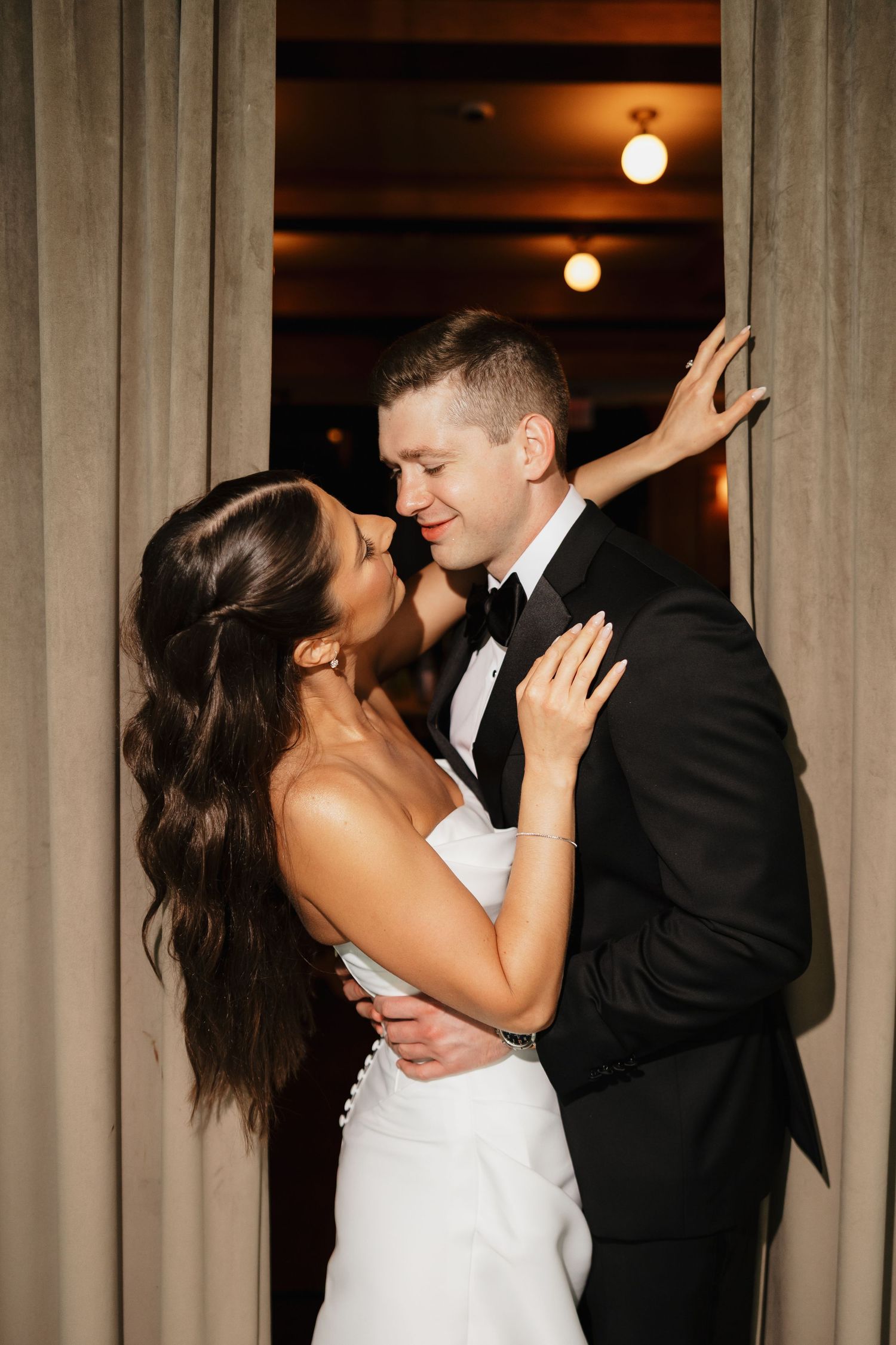 Bride and groom share an intimate moment in a doorway framed by elegant curtains.