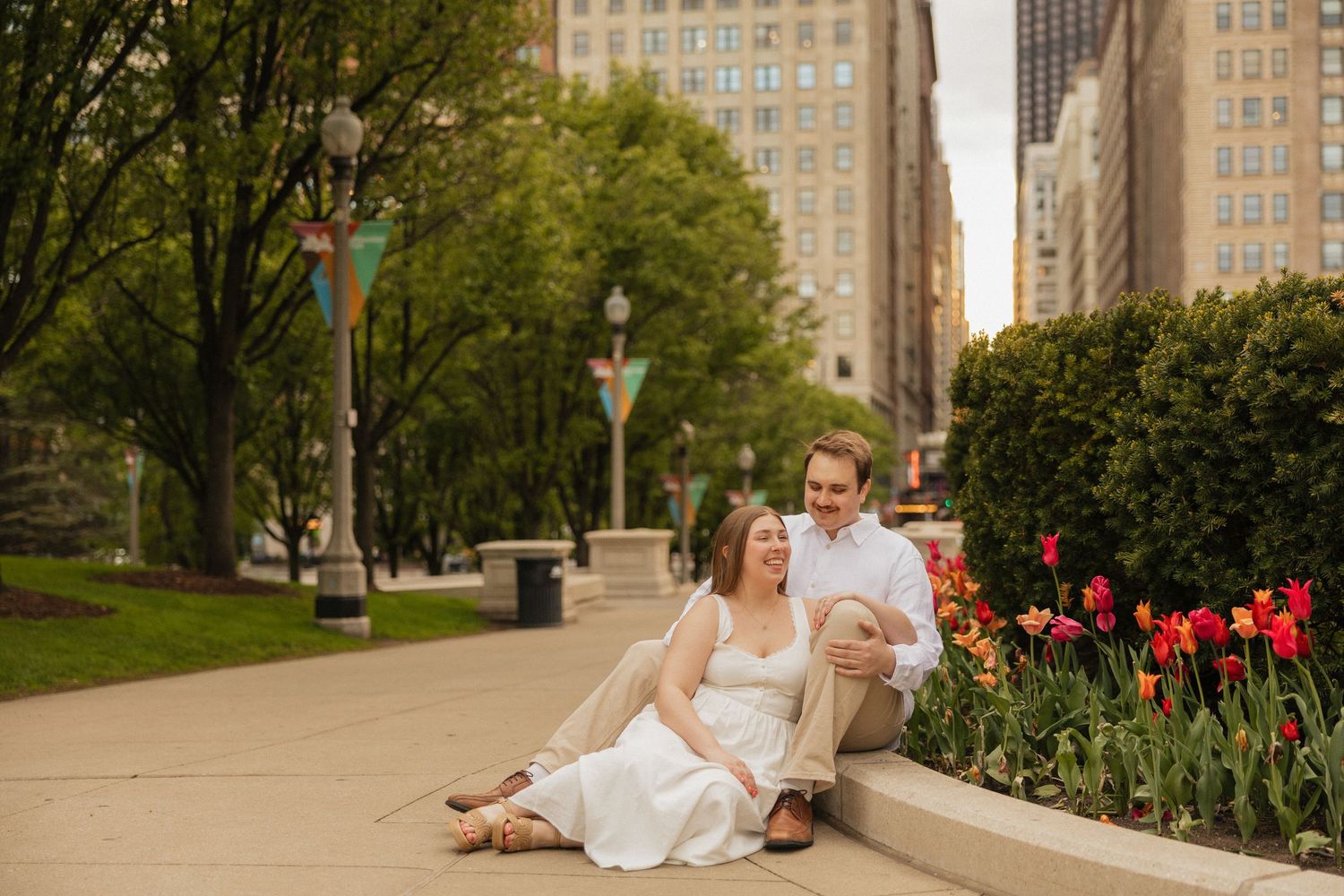 Couple sitting together in an urban park with red tulips and city buildings in the background on a spring day.