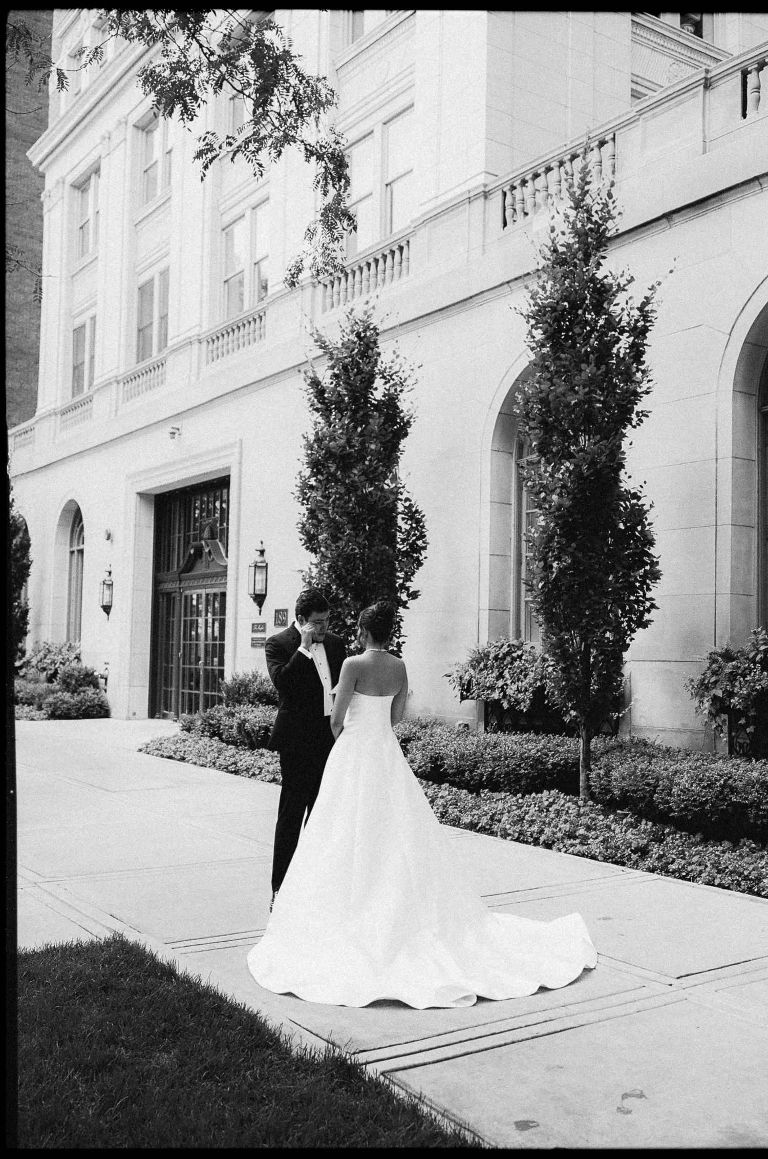Bride and groom sharing a romantic moment outside a grand classical building in black and white photo.