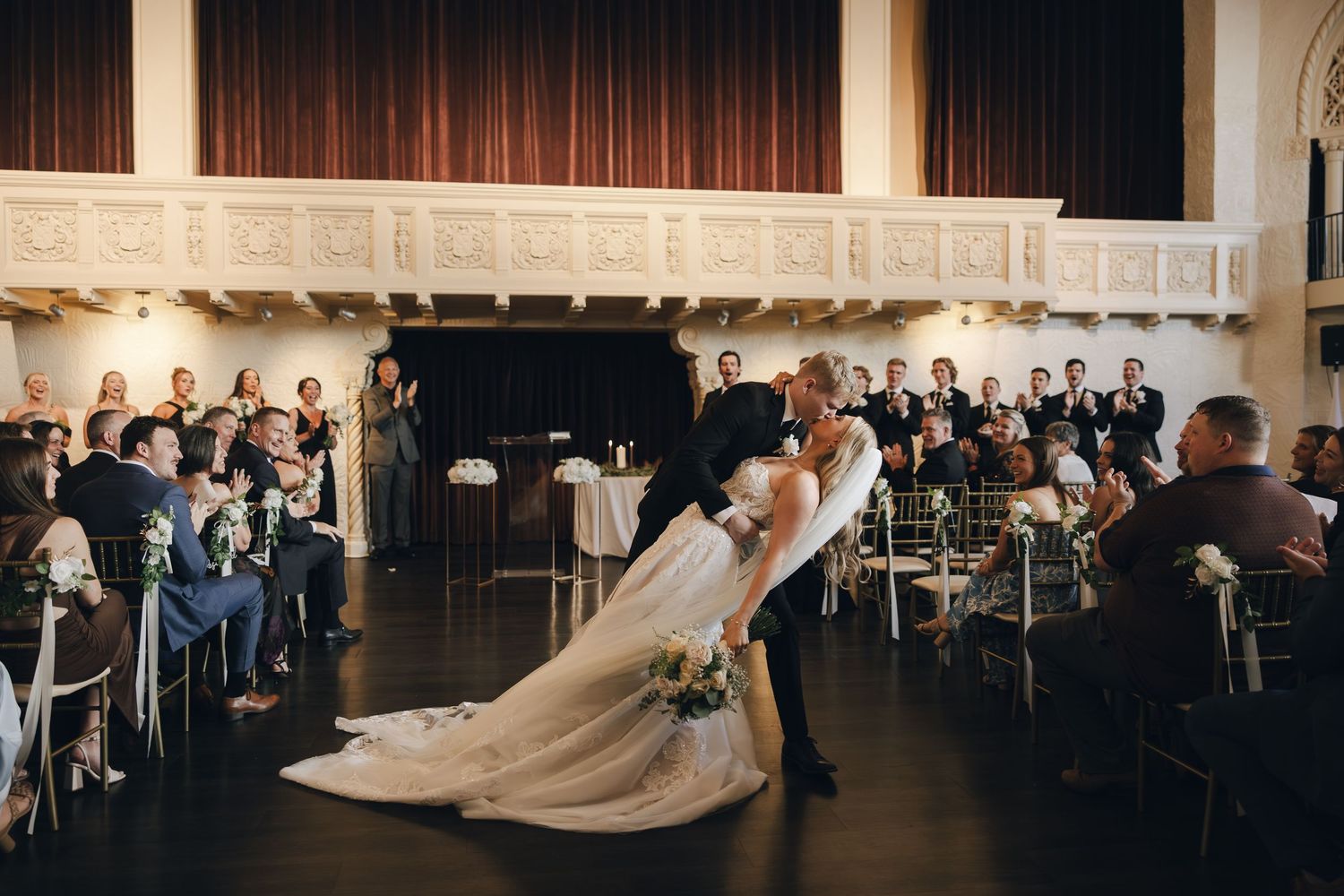 Wedding reception venue with elegant white drapery and chandeliers illuminating a spacious ballroom.