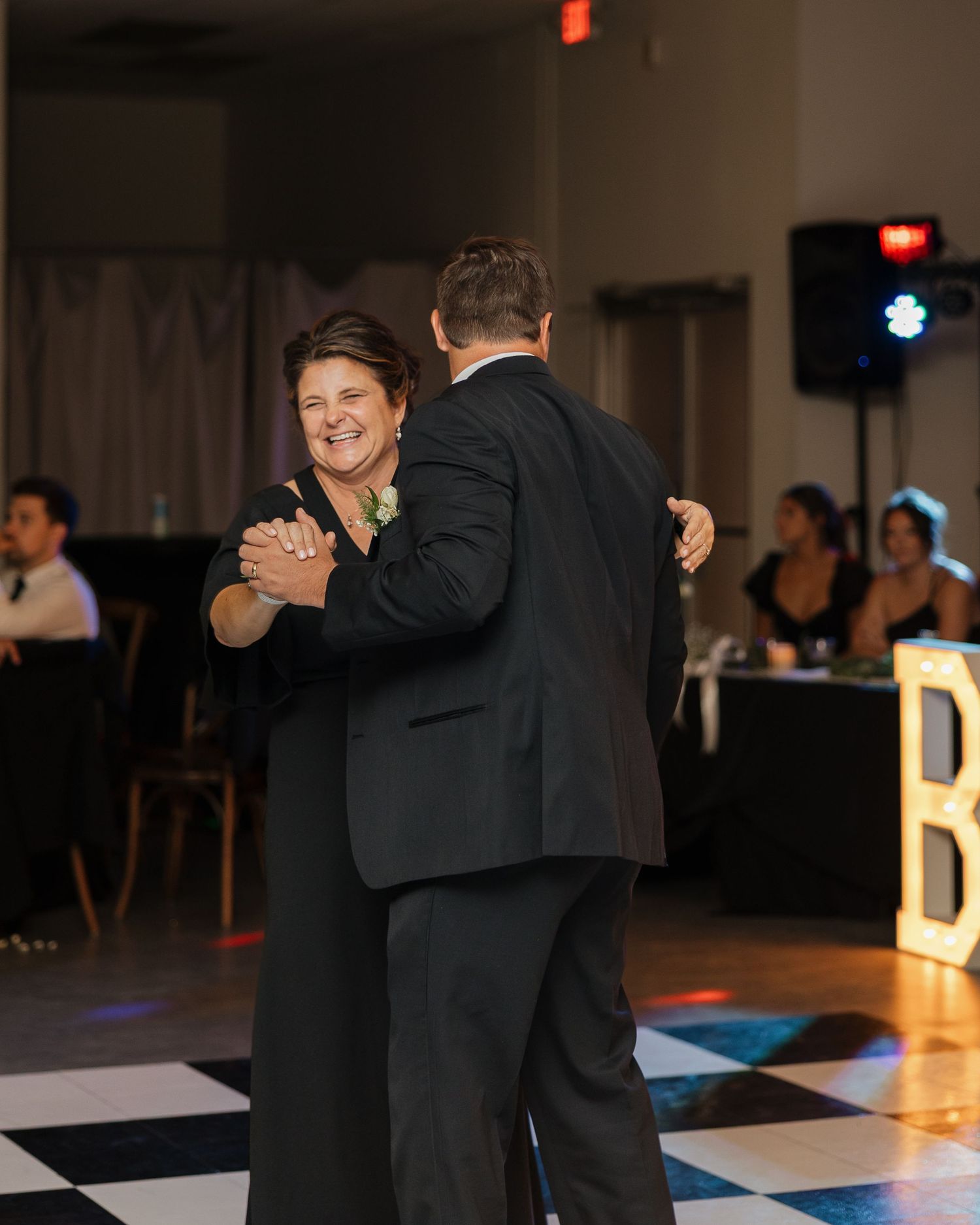 Wedding guests dancing and celebrating on a black and white checkered dance floor at an evening reception.
