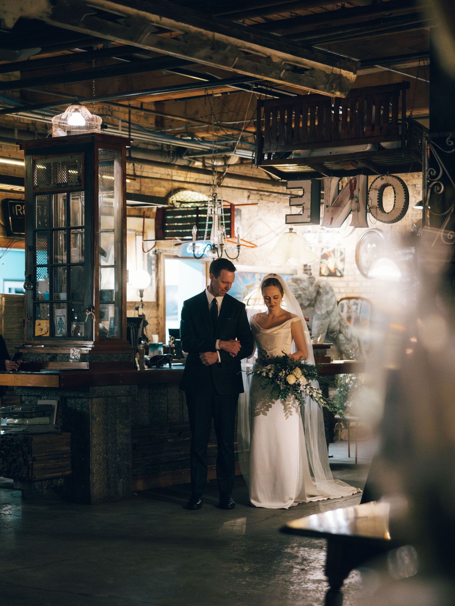 A couple shares a romantic dance in a rustic industrial venue with exposed beams and ambient lighting.