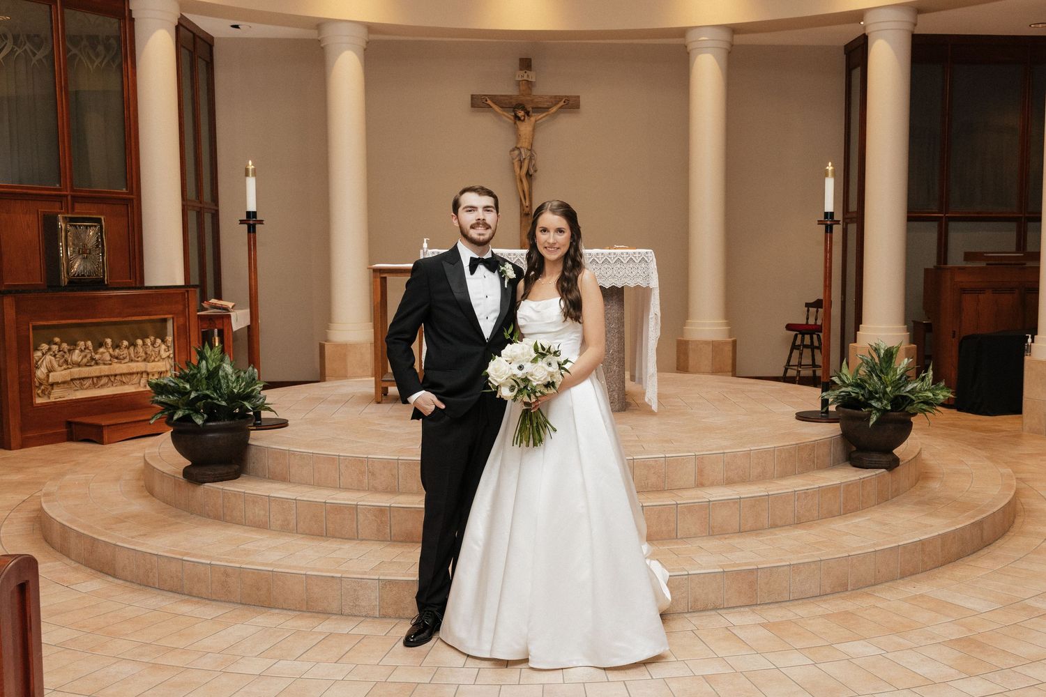 Bride and groom posing together at church altar after wedding ceremony, bride holding white bouquet.