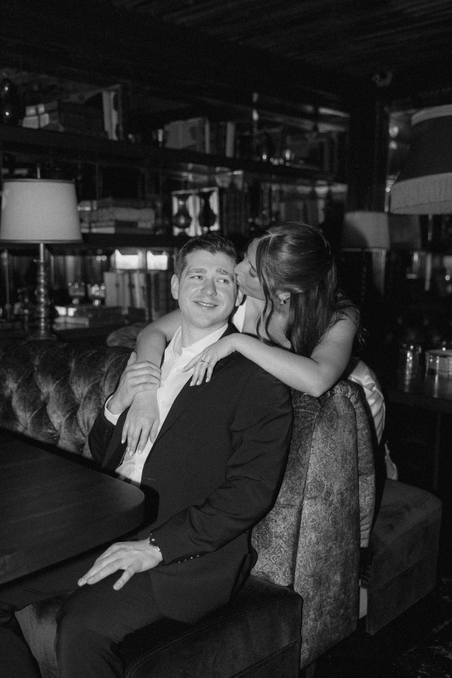 A couple lounges together on an ornate bench in a moody, dark setting.