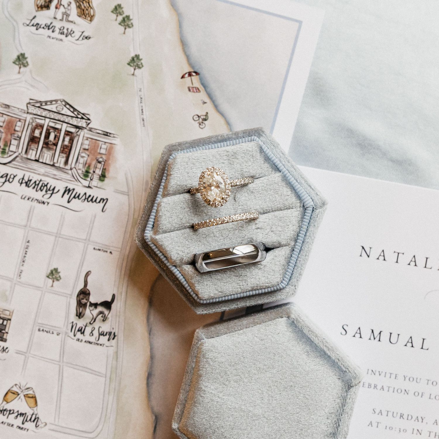 Wedding invitation suite with custom illustrations and calligraphy laid out on a white surface with hexagonal ring boxes.