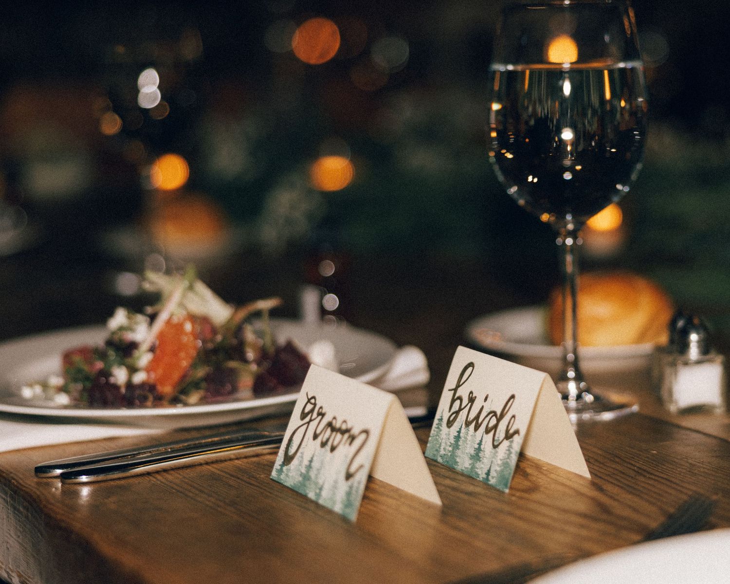 Place cards and table settings arranged on a wooden surface with bokeh lights in the background.