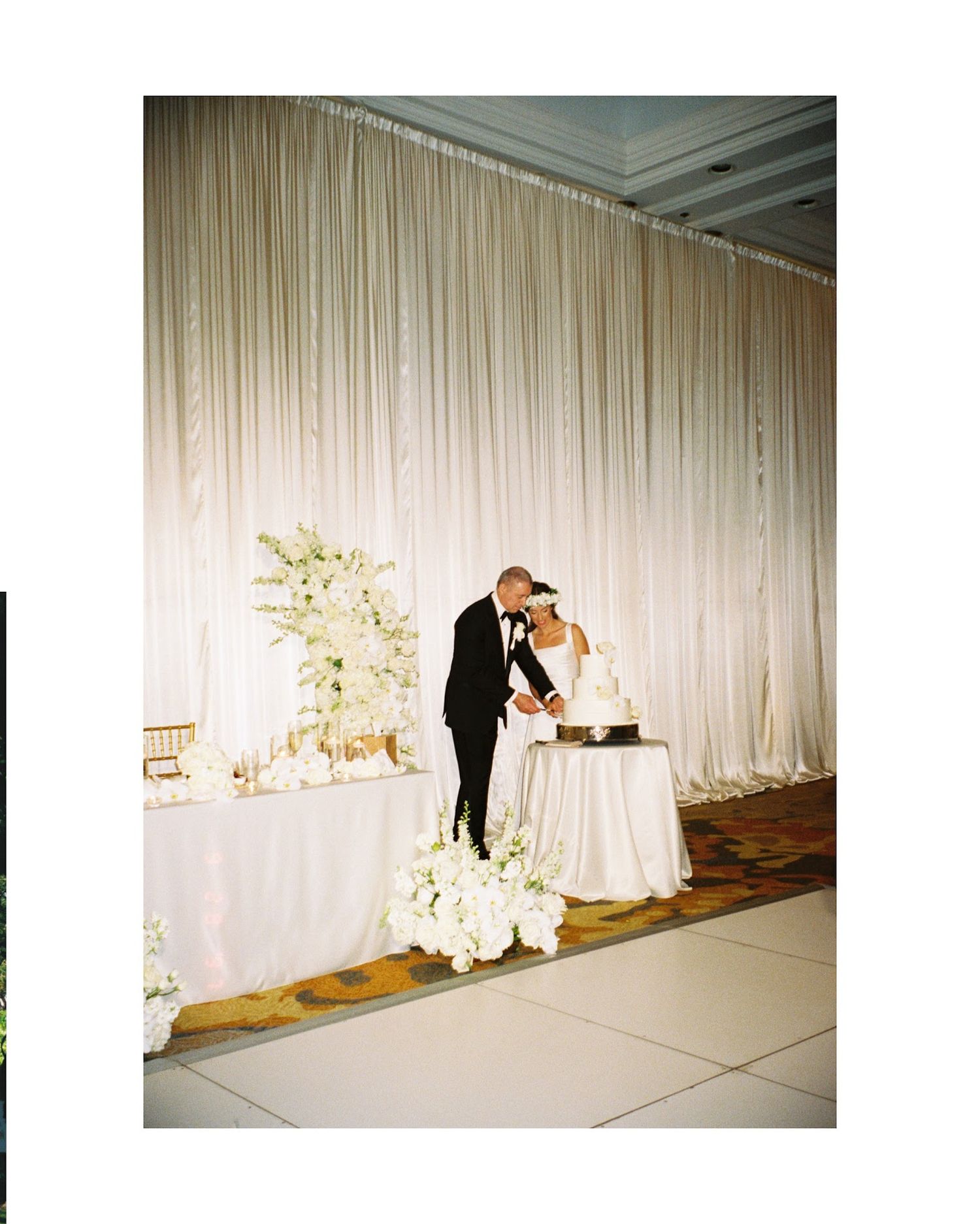A couple shares an intimate moment against a backdrop of elegant white drapes and floral arrangements at a wedding reception.