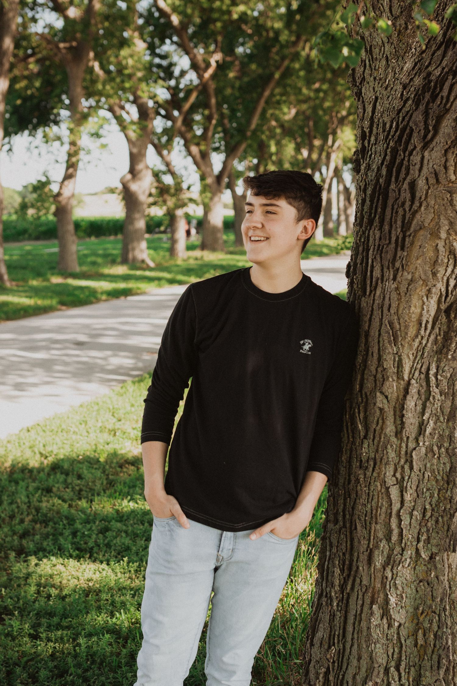 Casual outdoor portraits against tree trunks wearing black shirt and light jeans.