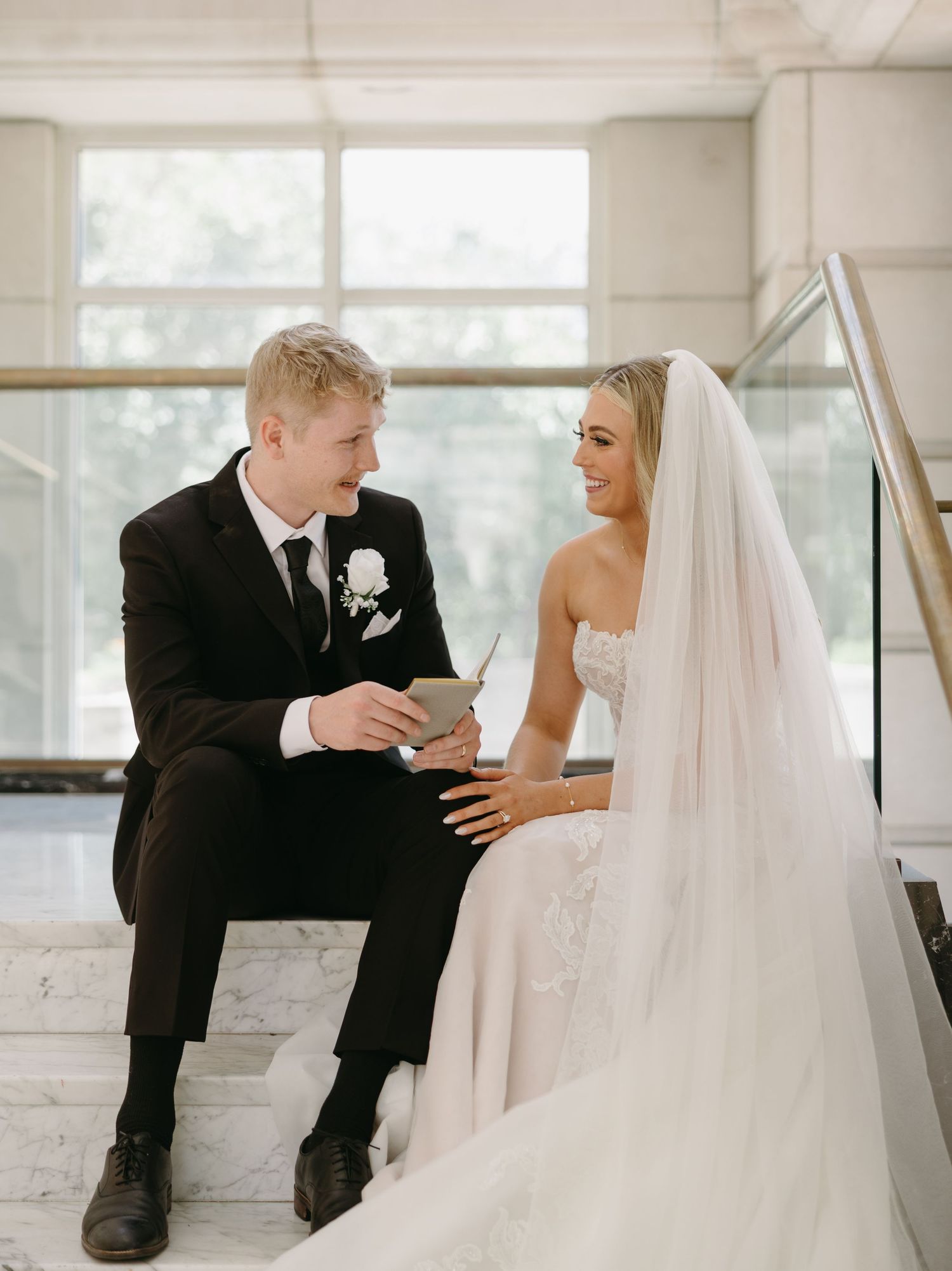 A bride and groom share intimate moments while sitting on white chairs in a bright, modern space.
