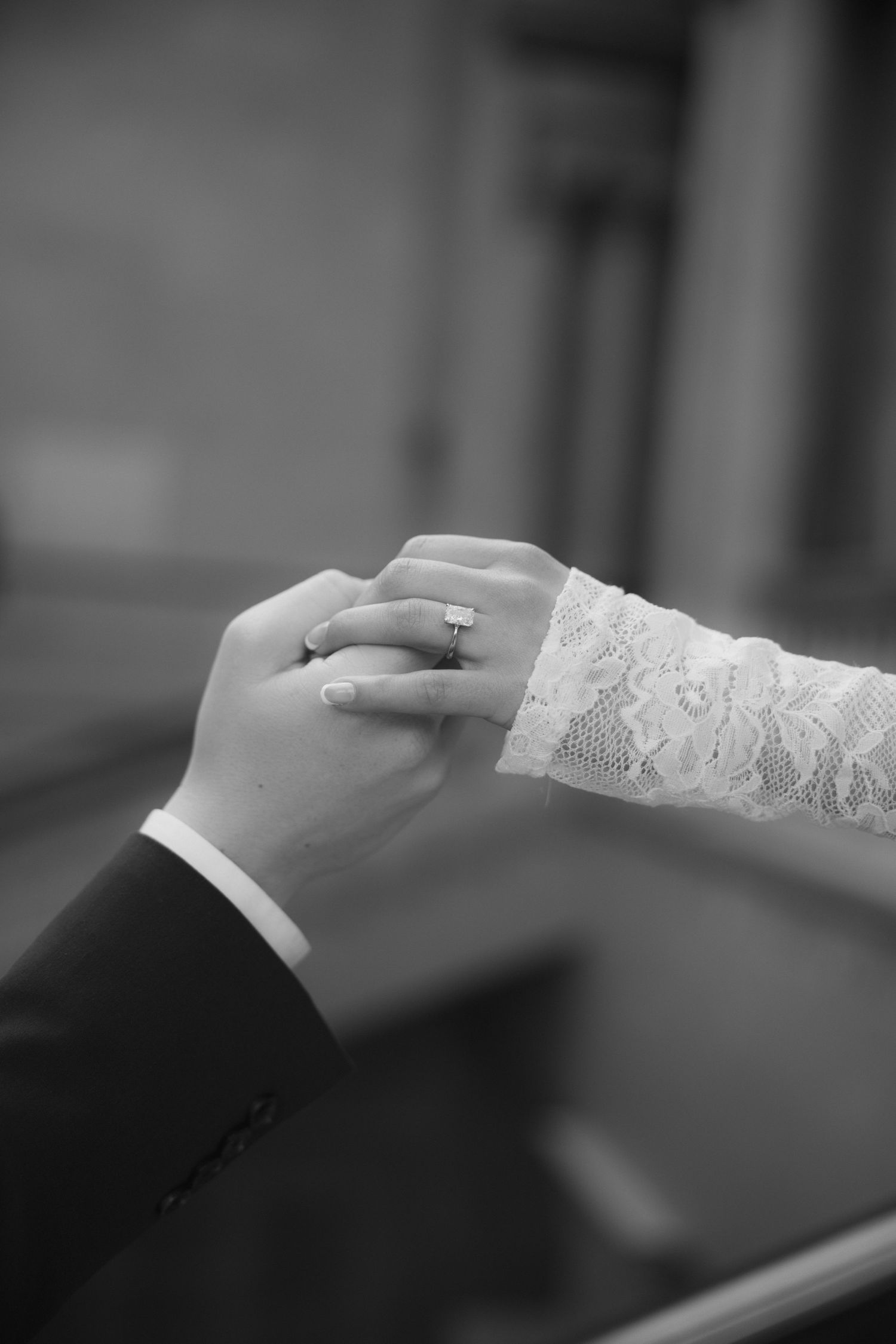 Close-up of hands with wedding rings and lace detail in black and white.