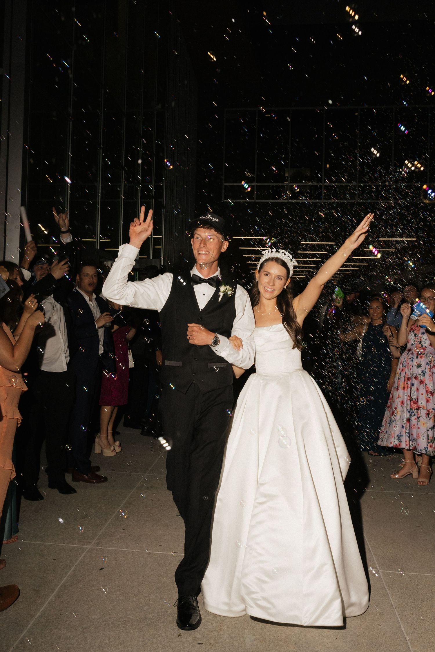 A joyful bride and groom celebrate their wedding exit with confetti, guests cheering around them in a festive night setting.