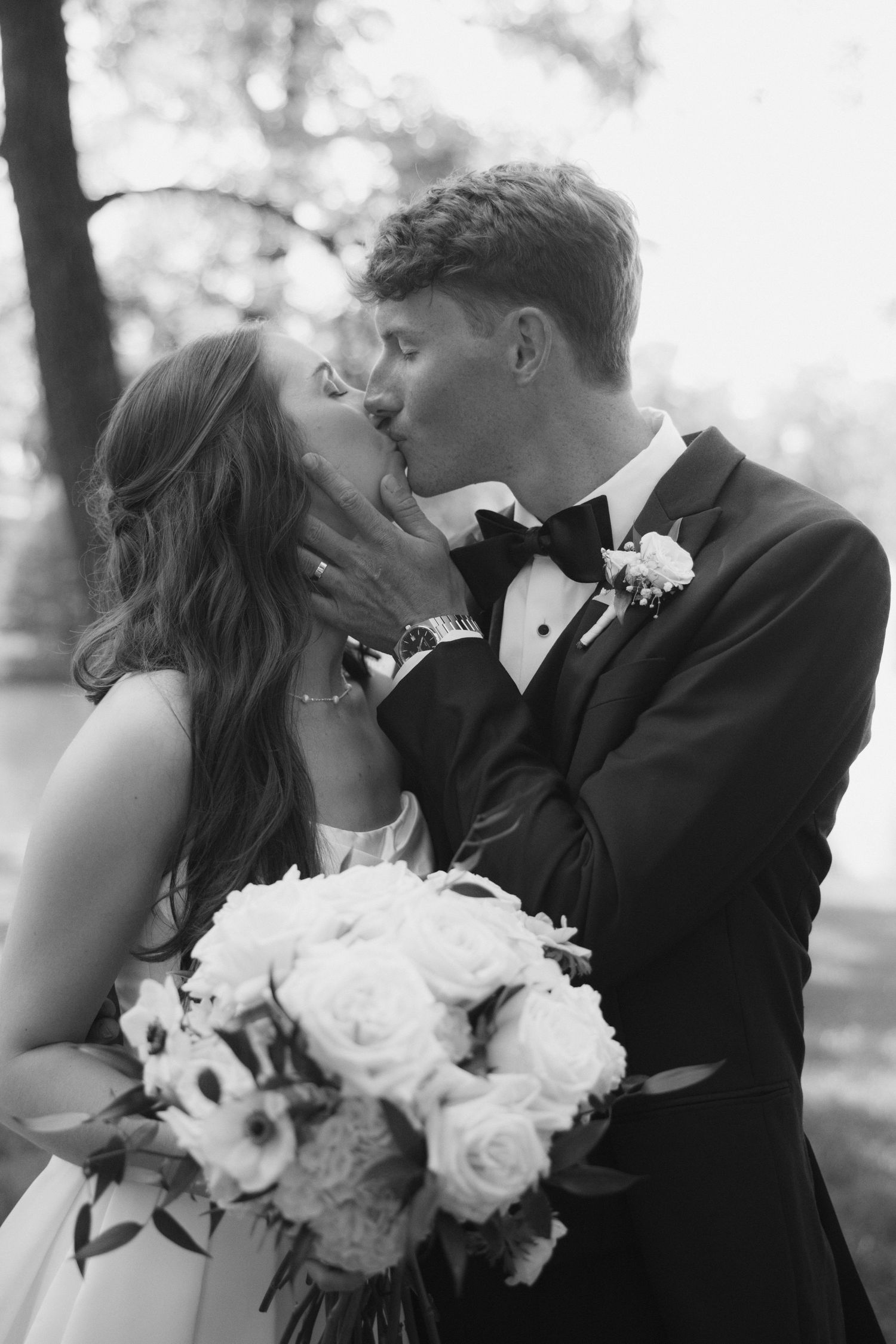 Black and white photo of a bride and groom sharing a romantic kiss, bride holding a bouquet of roses.
