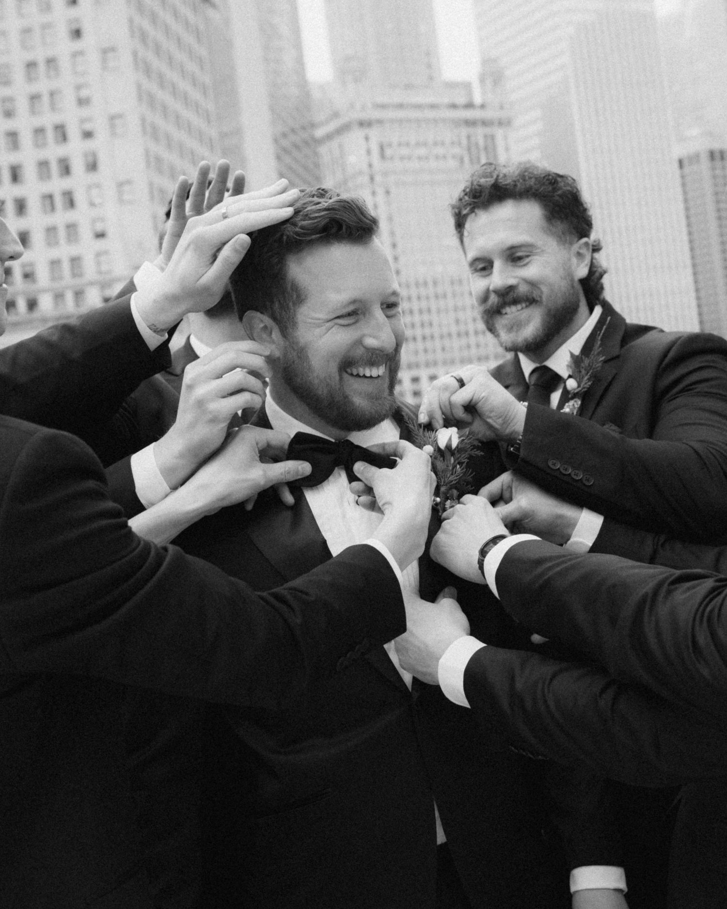 Black and white photo showing joyful moments between friends in formal attire against a city skyline backdrop.