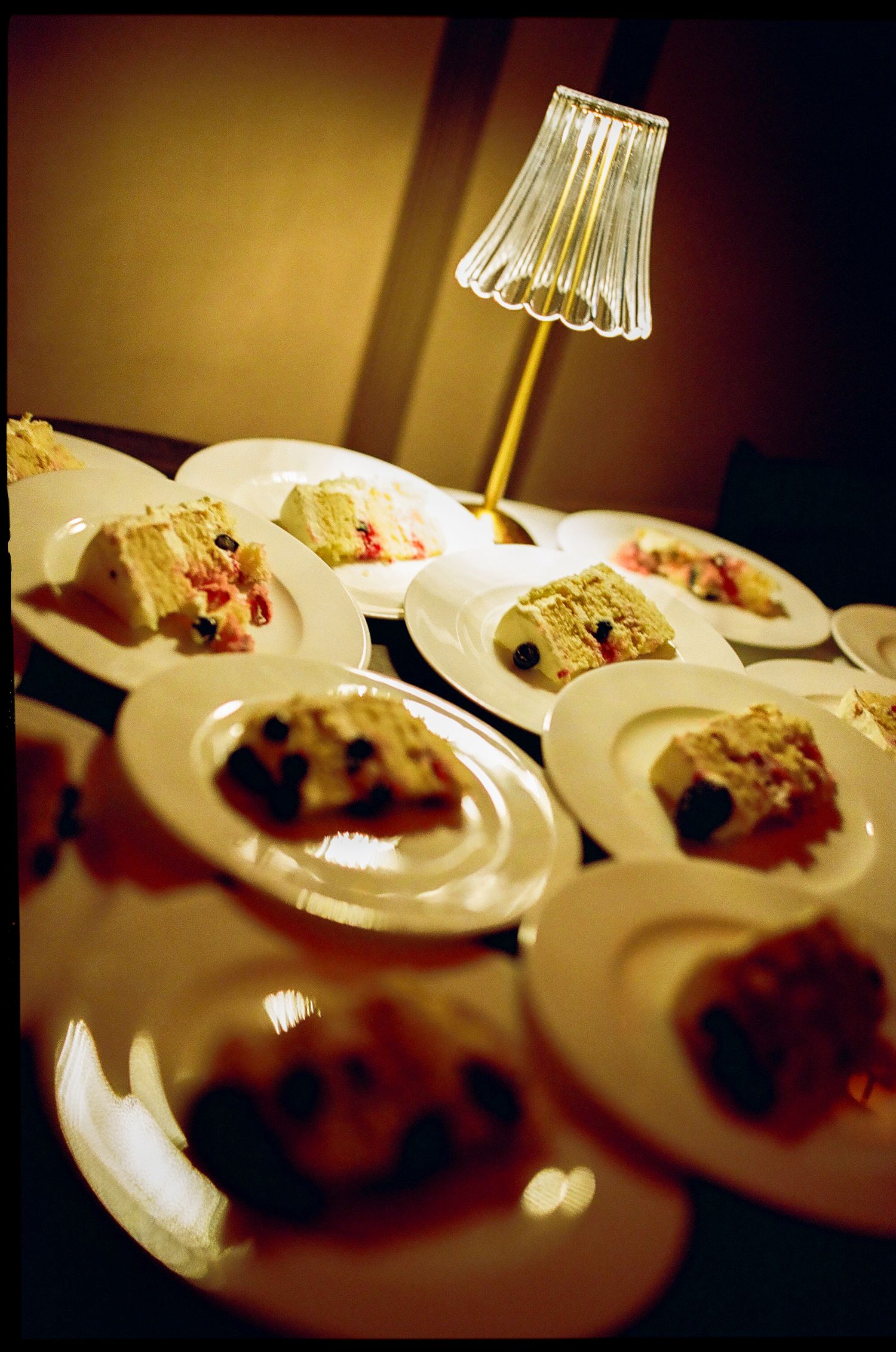 Wedding cake slices served on white plates beside decorative crystal lamp at elegant reception.