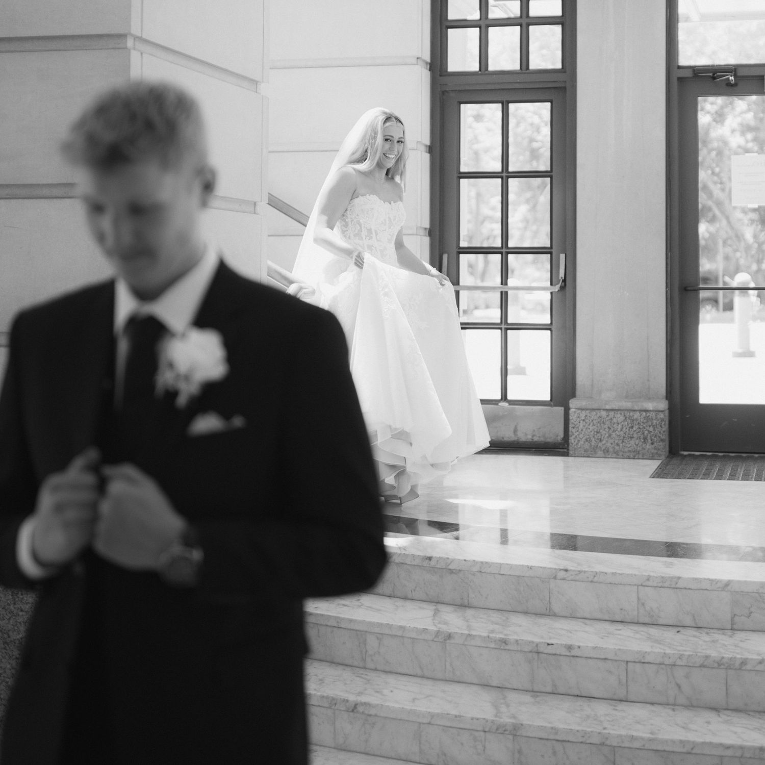 Person in formal black attire stands near a window in a bright interior space.