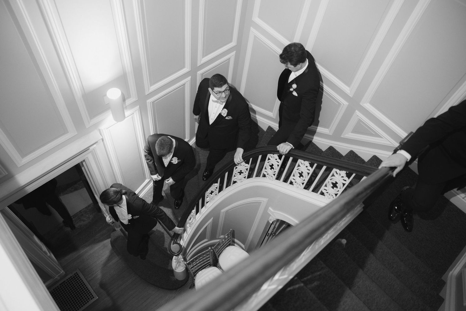 Black and white photo of groomsmen gathered on an elegant staircase during a wedding day preparation.