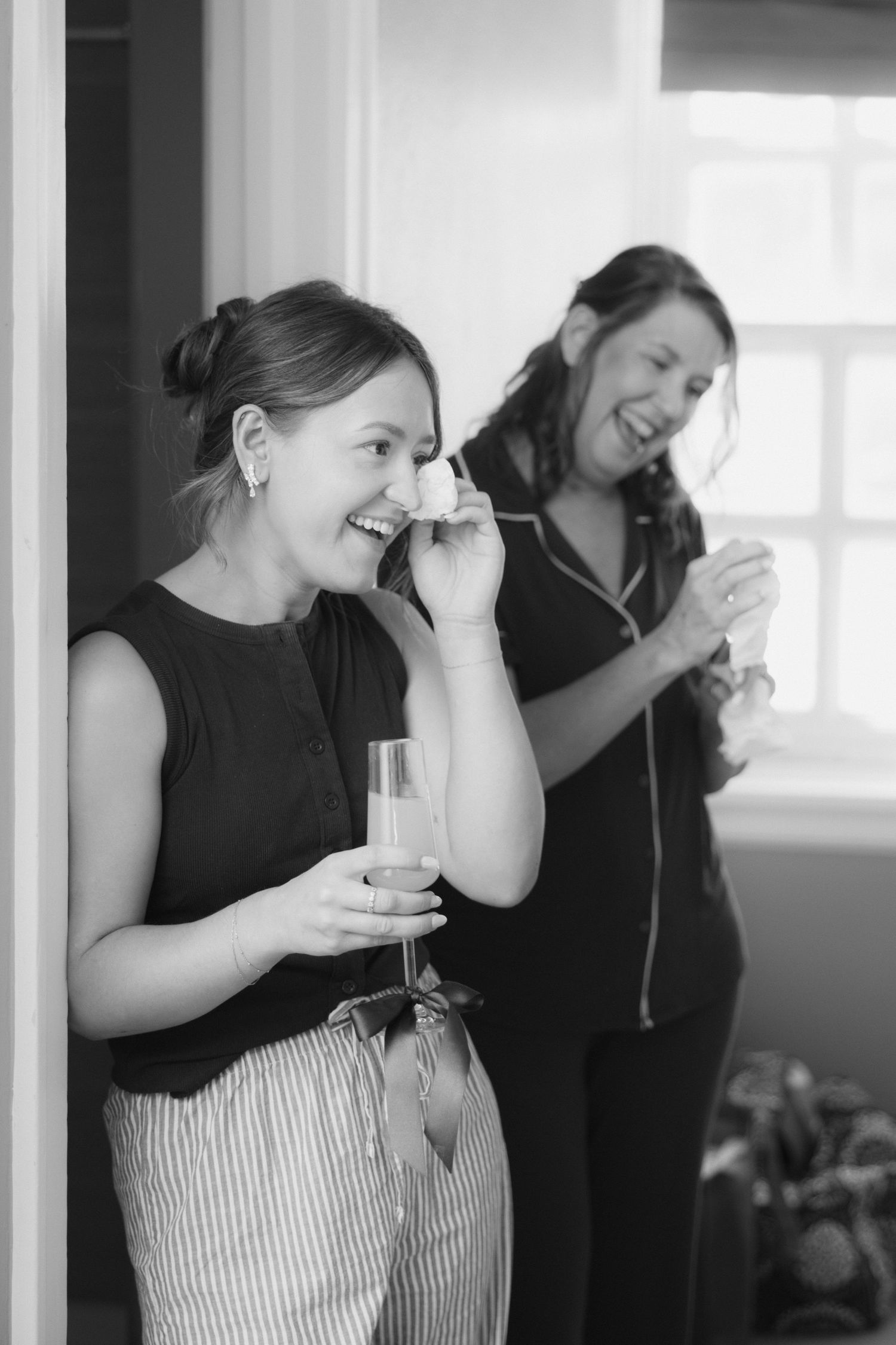 Two women laughing and holding champagne glasses in a black and white photo at a celebratory event.