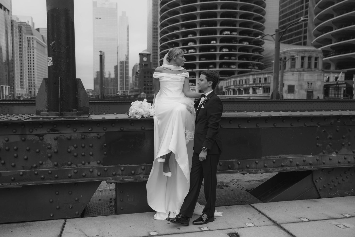 Bride and groom share a romantic moment on a Chicago bridge with city skyline in black and white.