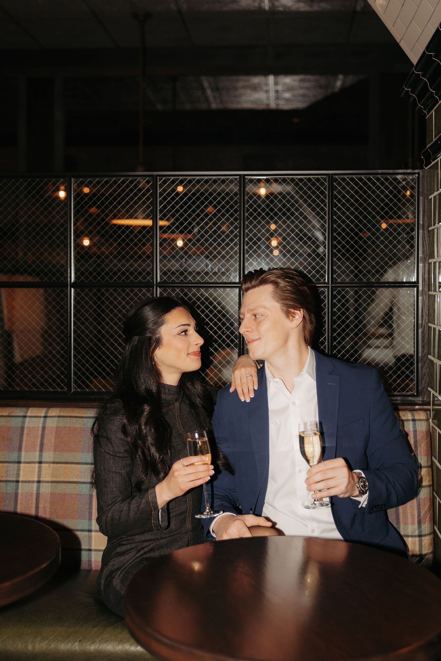 A couple shares drinks and intimate moments at a dimly lit restaurant booth.