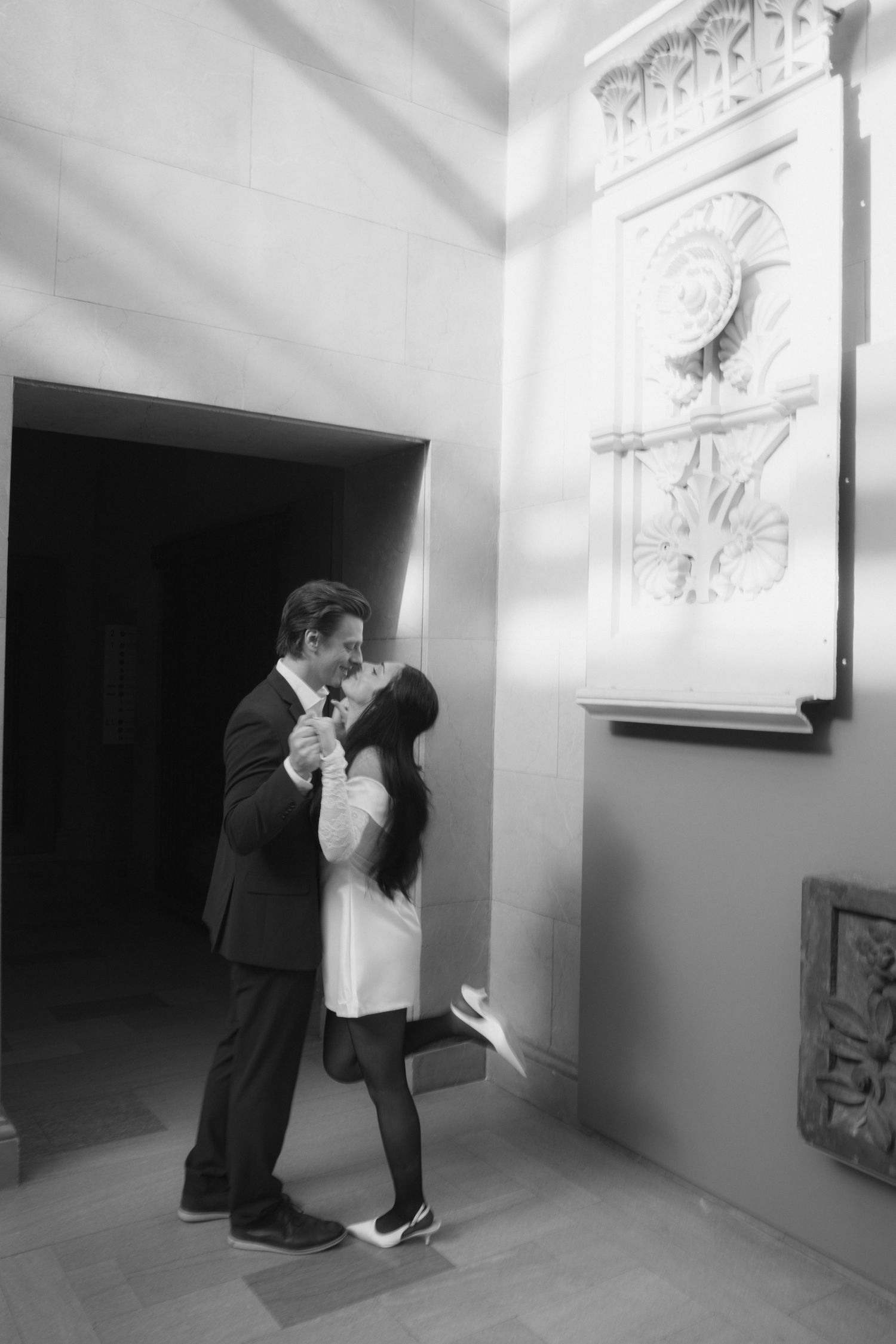 A couple shares a romantic moment in a minimalist white gallery space with artwork.