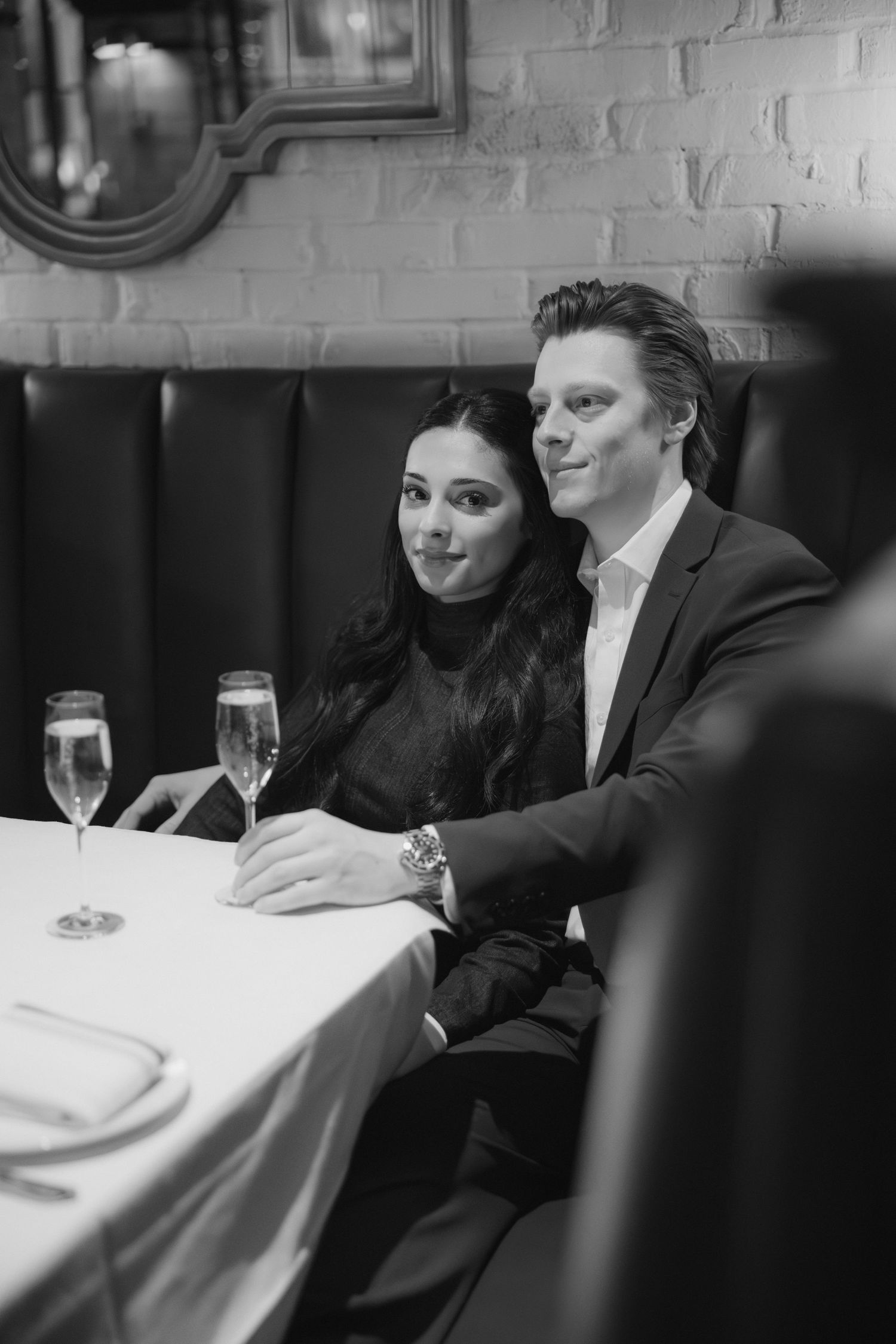 Business professionals in formal attire sit at a table during a meeting or dinner event.