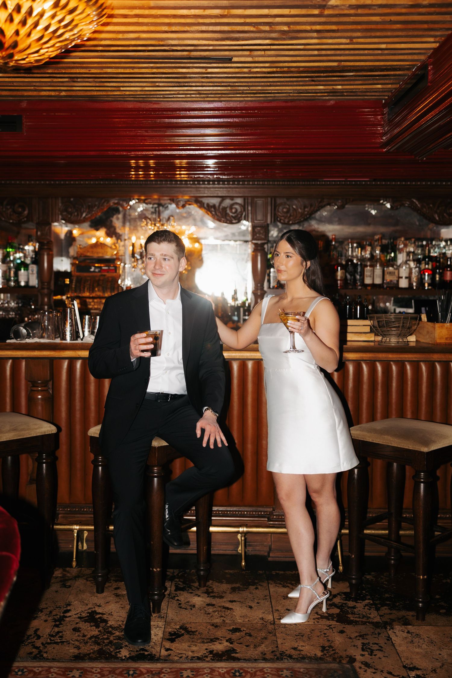 A couple in contrasting black and white outfits enjoying cocktails at a luxurious bar.