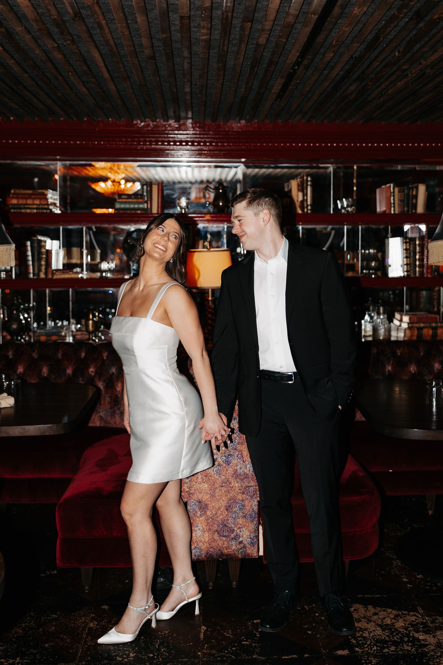 A couple in formal attire dances together in a dimly lit venue with wooden beams overhead.