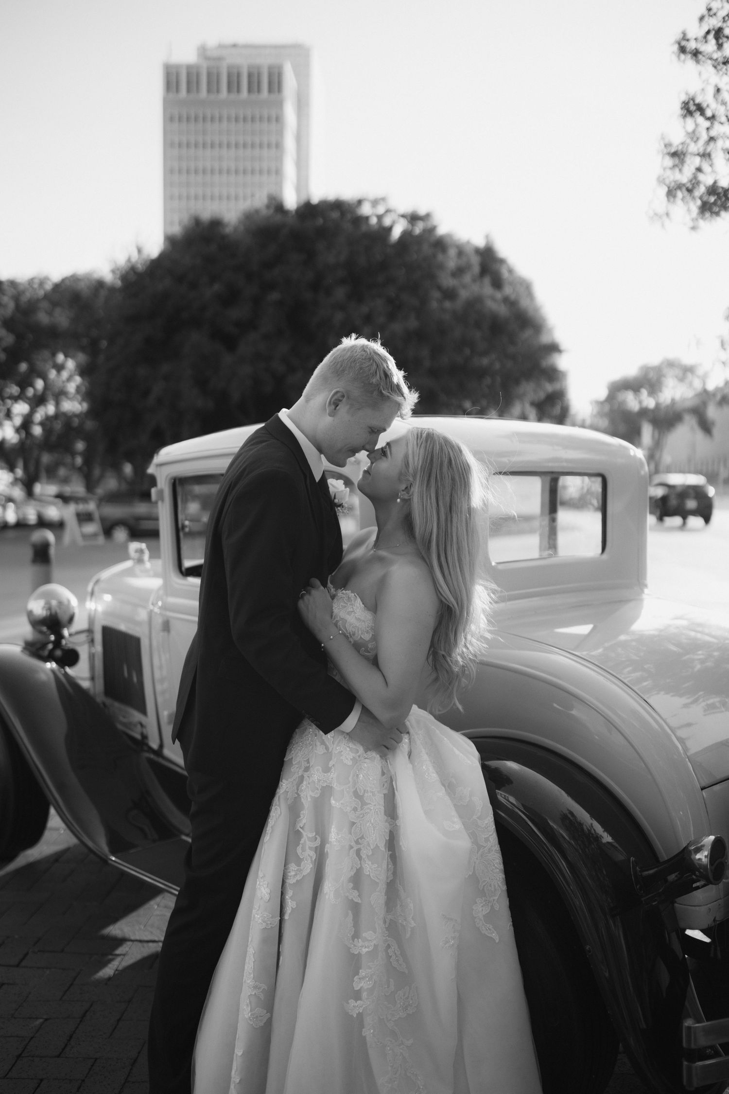 Couple sharing a romantic moment next to a classic car outdoors.