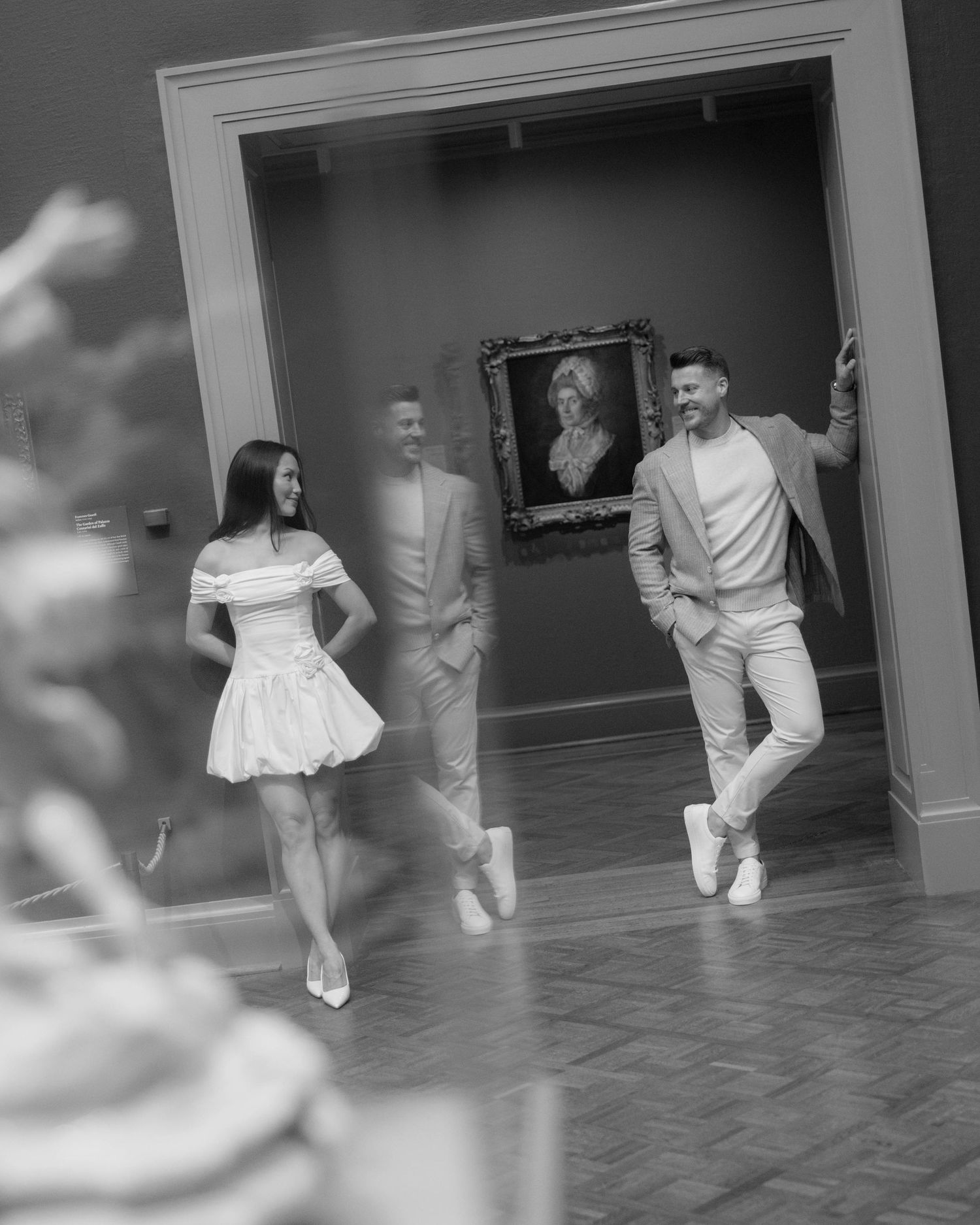 Black and white photo of a couple walking through an art museum gallery with a portrait painting on the wall.