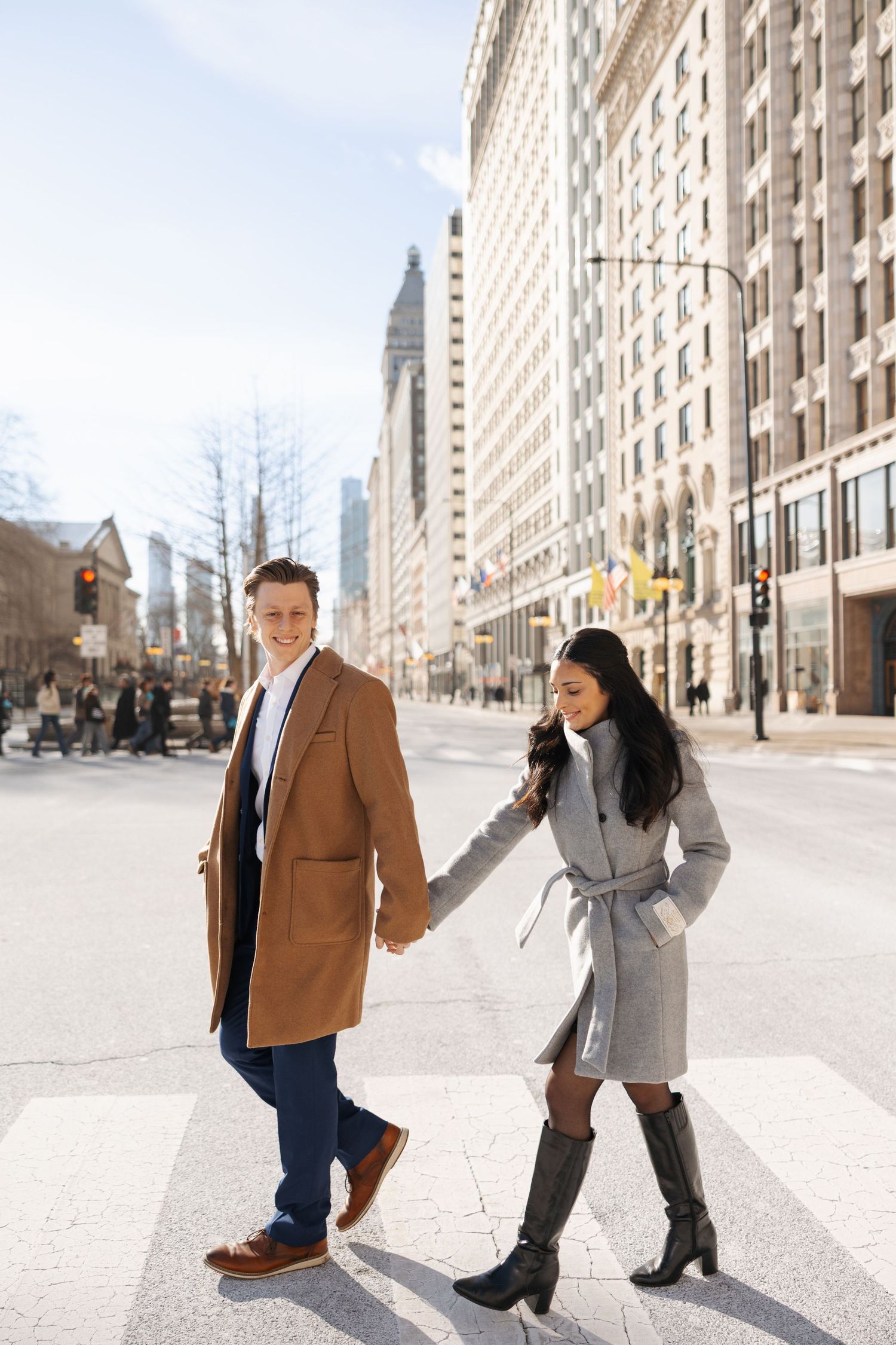 A couple walks hand in hand down a sunny city street lined with tall buildings.