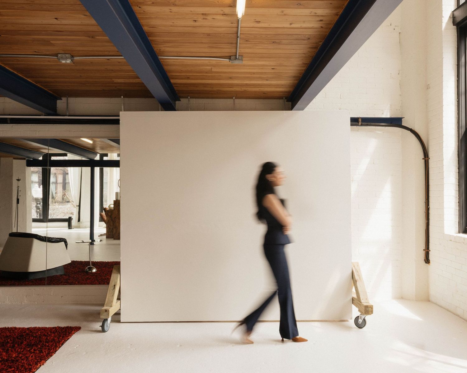 Woman walking past a large white movable partition wall in a modern loft office space with wood ceiling.