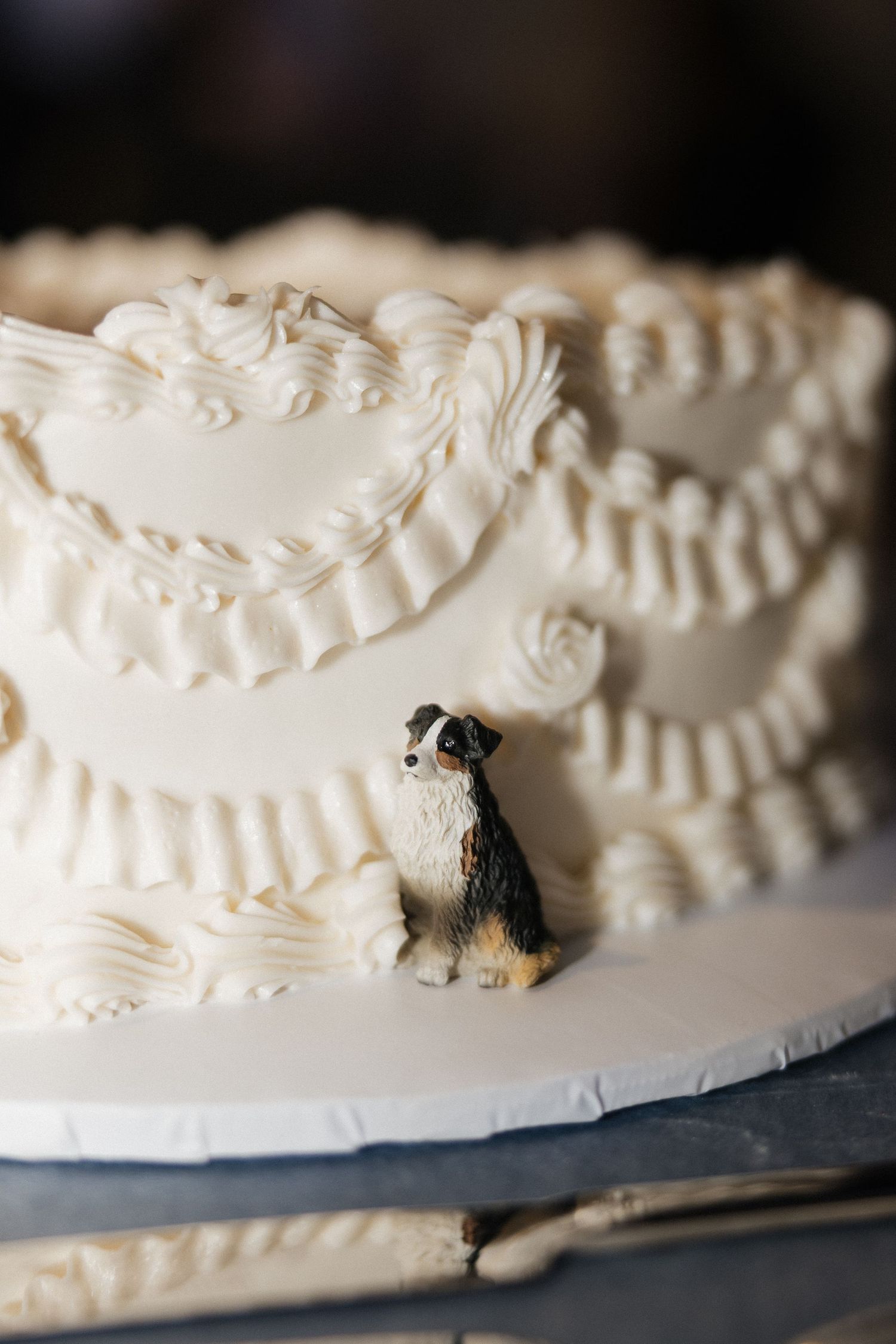 White wedding cake with intricate frosting details and a small dog figurine topper on a slate board.