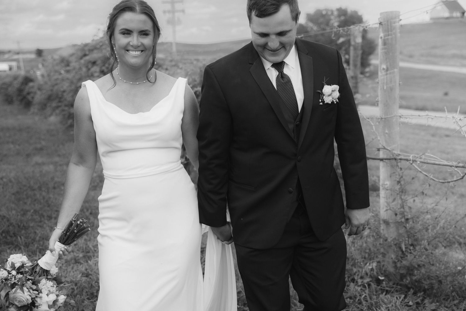 A wedding party in formal attire poses outdoors with the bride in white and groomsmen in black suits.