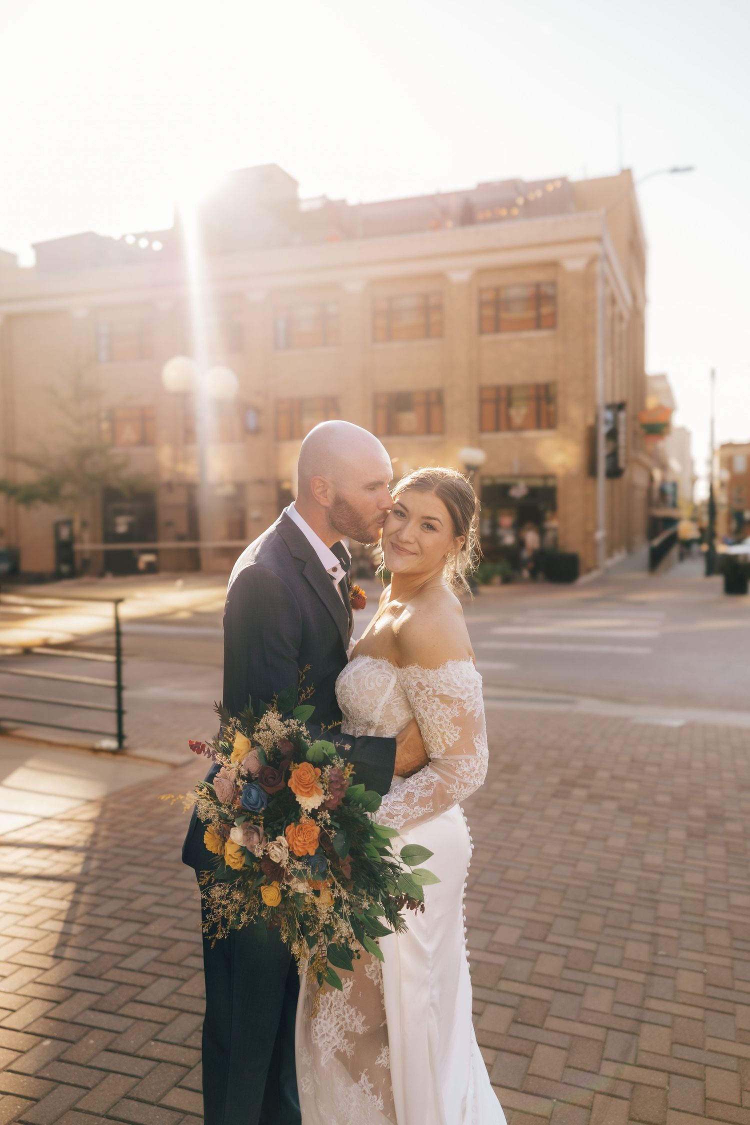 Newlyweds share an intimate moment at sunset on brick pavers with a beautiful floral bouquet.