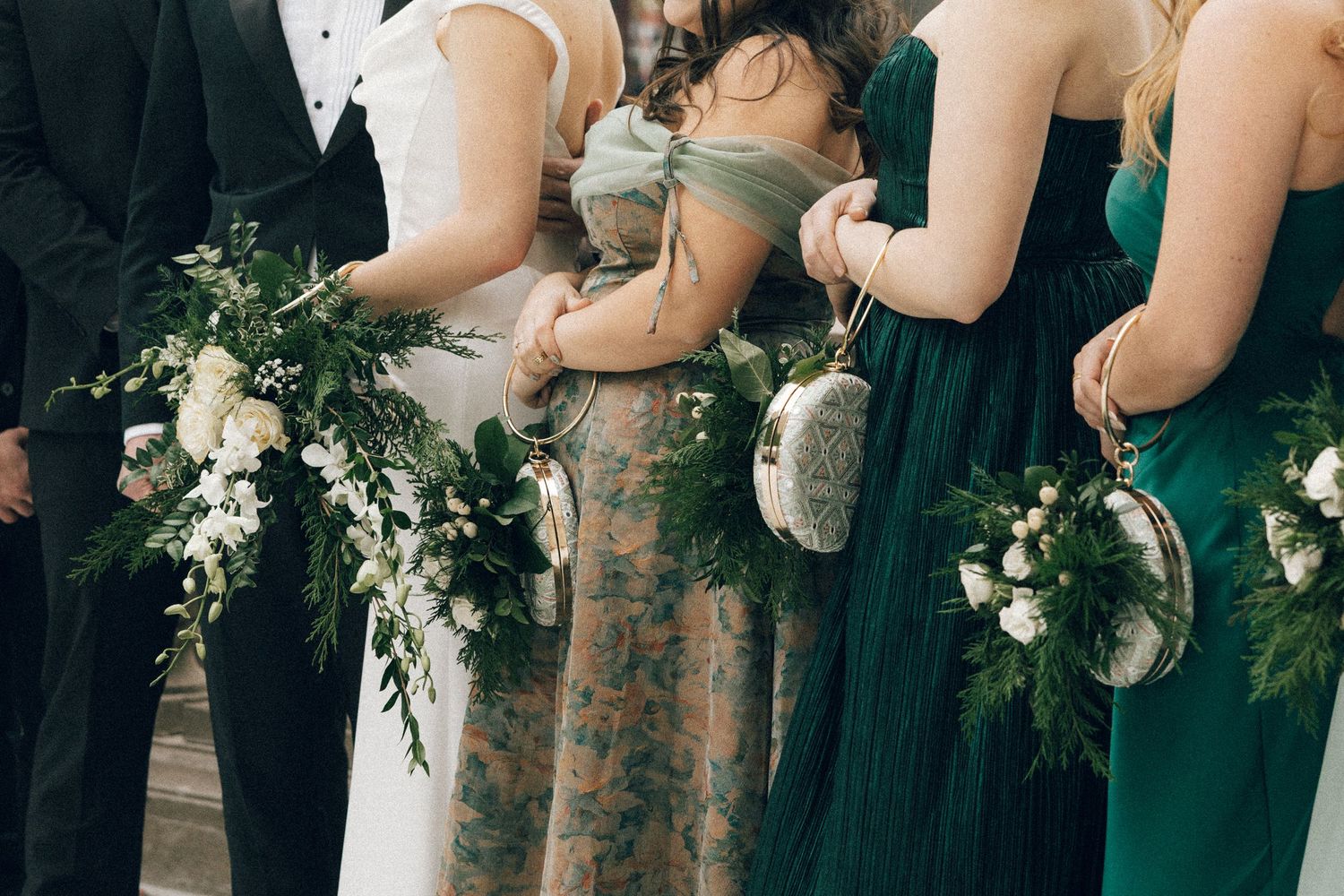 A row of bridesmaids in dark green dresses hold white and green floral bouquets at a formal wedding ceremony.