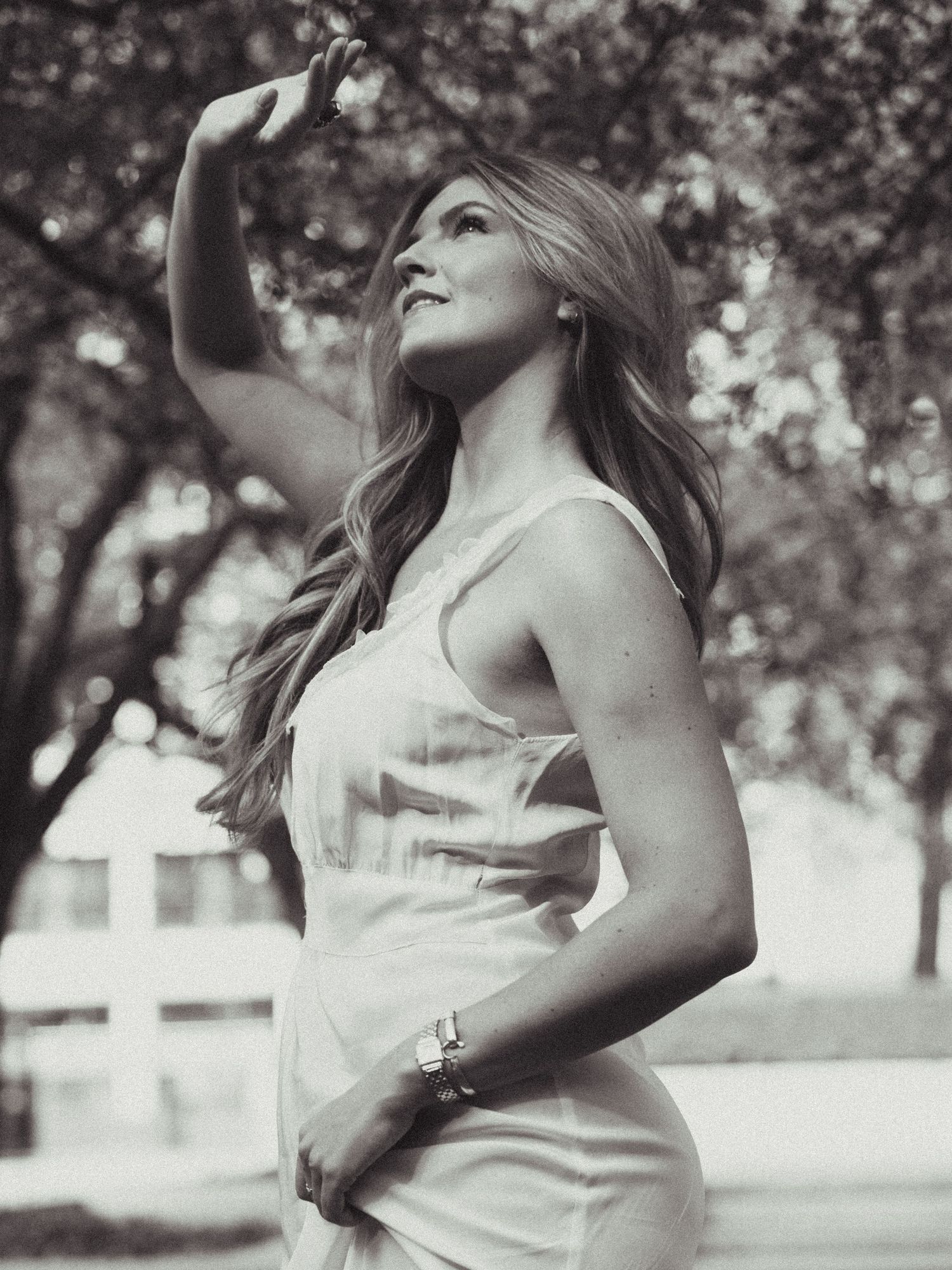 Black and white photo of a woman in a white dress posing outdoors with trees in the background.