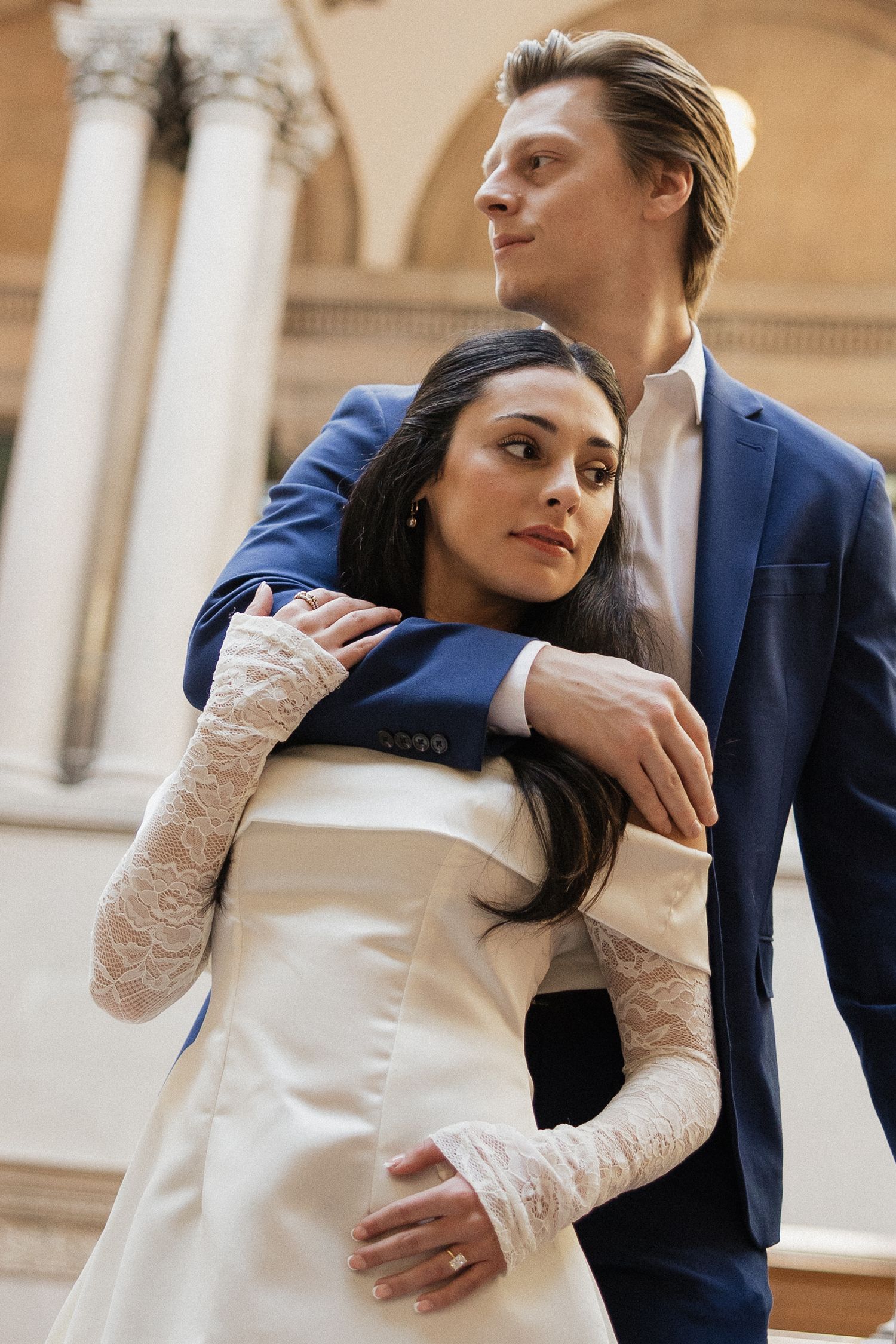 Two people embrace in a romantic pose against a classical architectural backdrop with columns.