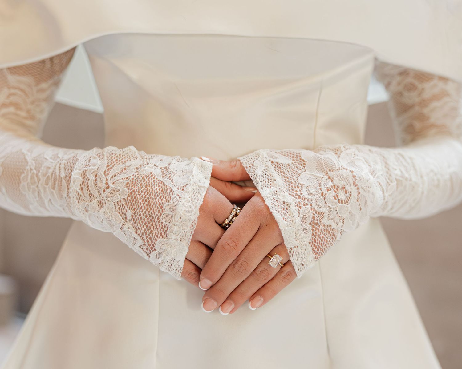 Elegant white lace fingerless gloves worn with a wedding dress, hands clasped gracefully at the waist.