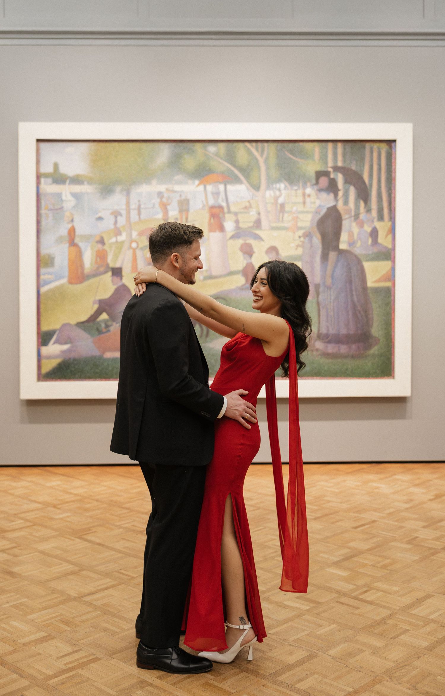 A couple in formal attire dances in an art gallery in front of Georges Seurat's 'A Sunday Afternoon' painting.