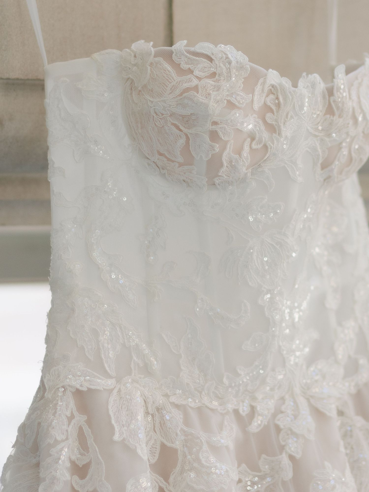 Close-up of an elegant strapless wedding dress featuring intricate beaded lace appliques in ivory and blush pink.