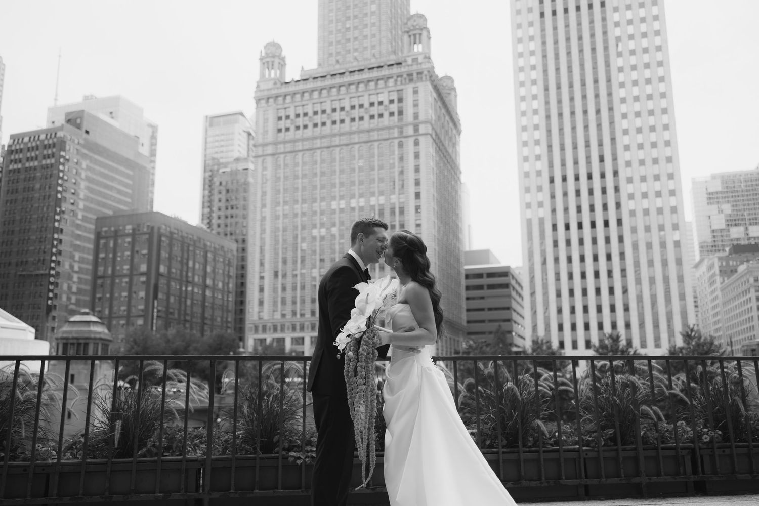 Black and white photo of a bride and groom kissing in front of a city skyline on their wedding day.