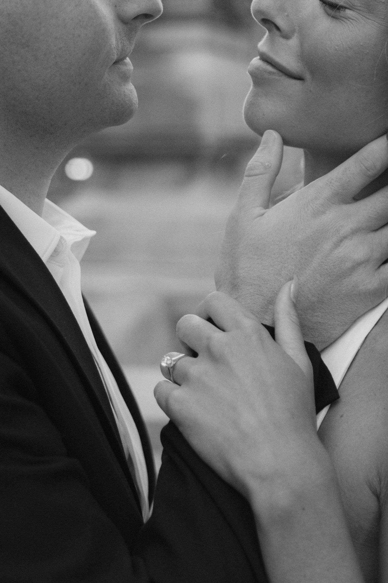Black and white photo of a couple in formal wear about to kiss, woman wearing a diamond engagement ring.