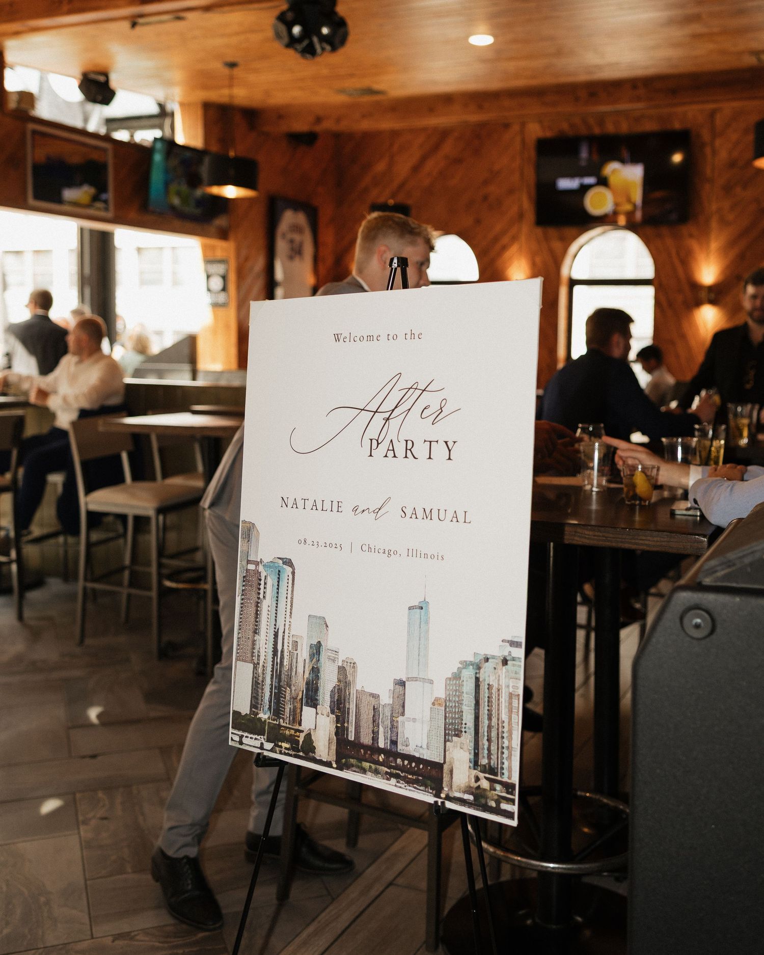 Wedding reception signage and decor with cityscape artwork displayed in a rustic wooden venue.
