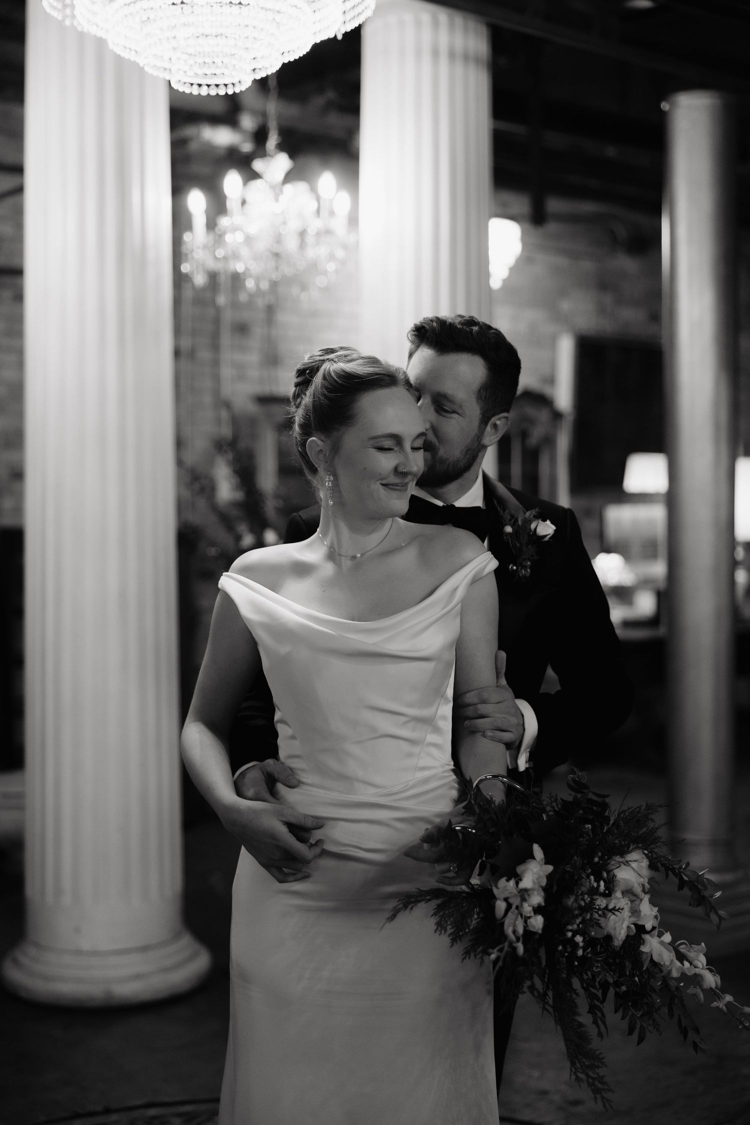 A romantic black and white wedding portrait series showing intimate moments between newlyweds near classic columns.