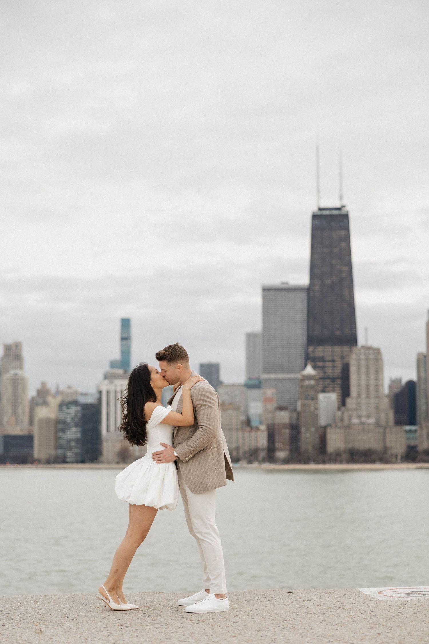 Couple sharing a romantic kiss on Chicago lakefront with city skyline and skyscrapers in background.