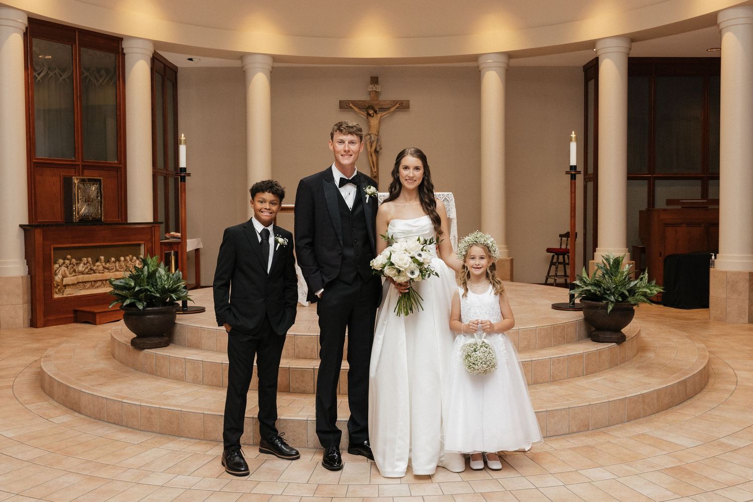 Bride and groom pose with young ring bearer and flower girl inside an elegant church chapel after their wedding ceremony.