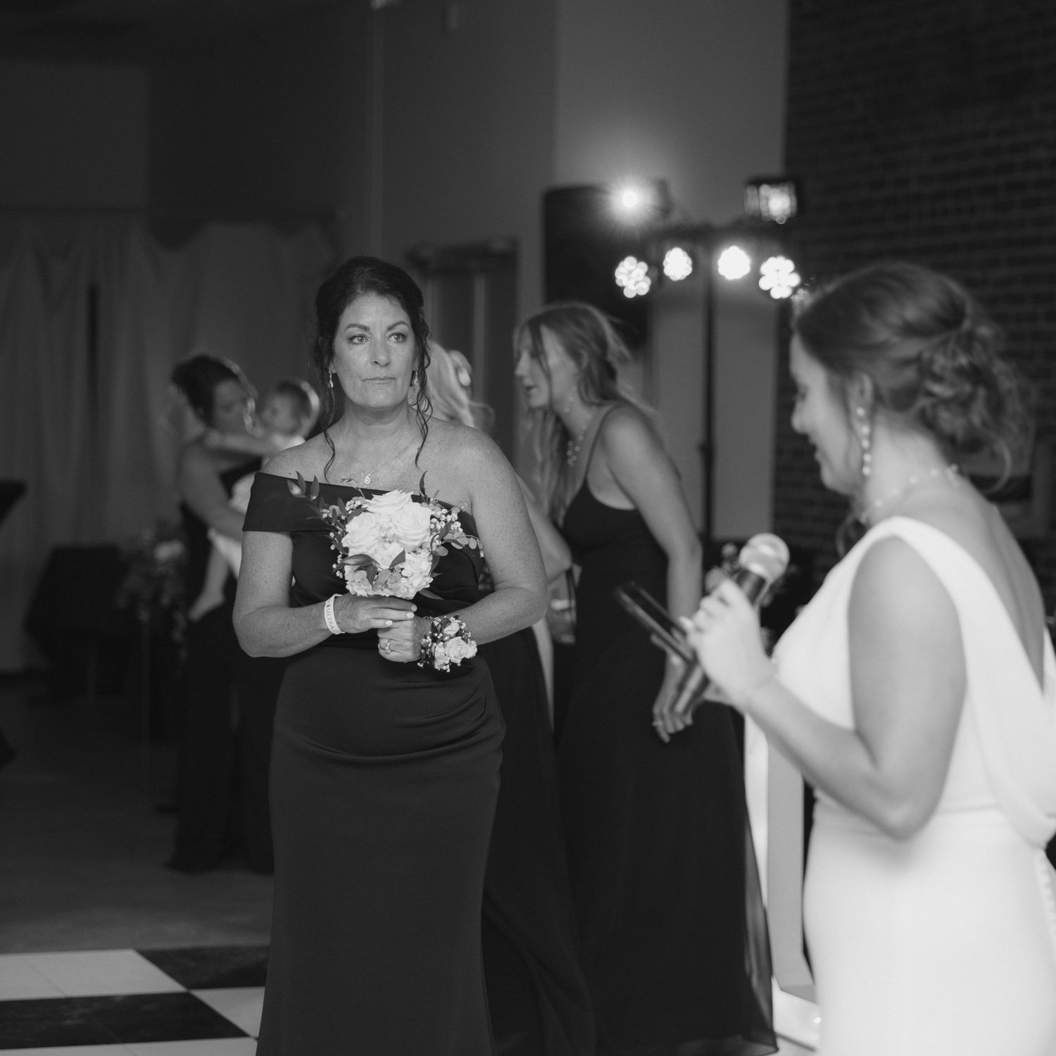 Wedding guests dancing and socializing on a checkered dance floor at an indoor reception venue.