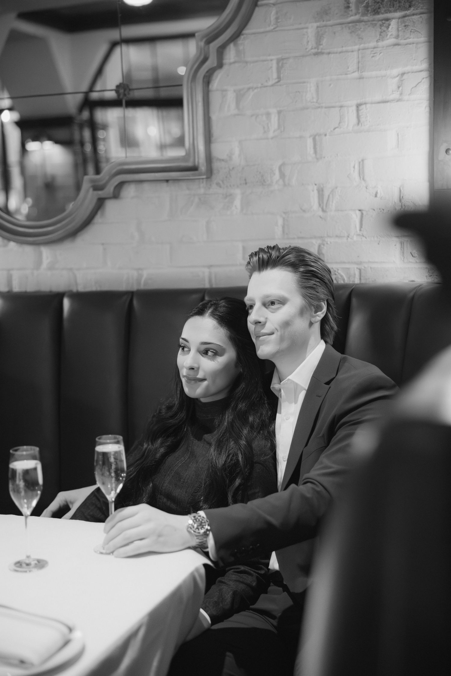 Couple in formal attire enjoying an elegant dinner at a white-tablecloth restaurant with wine glasses.