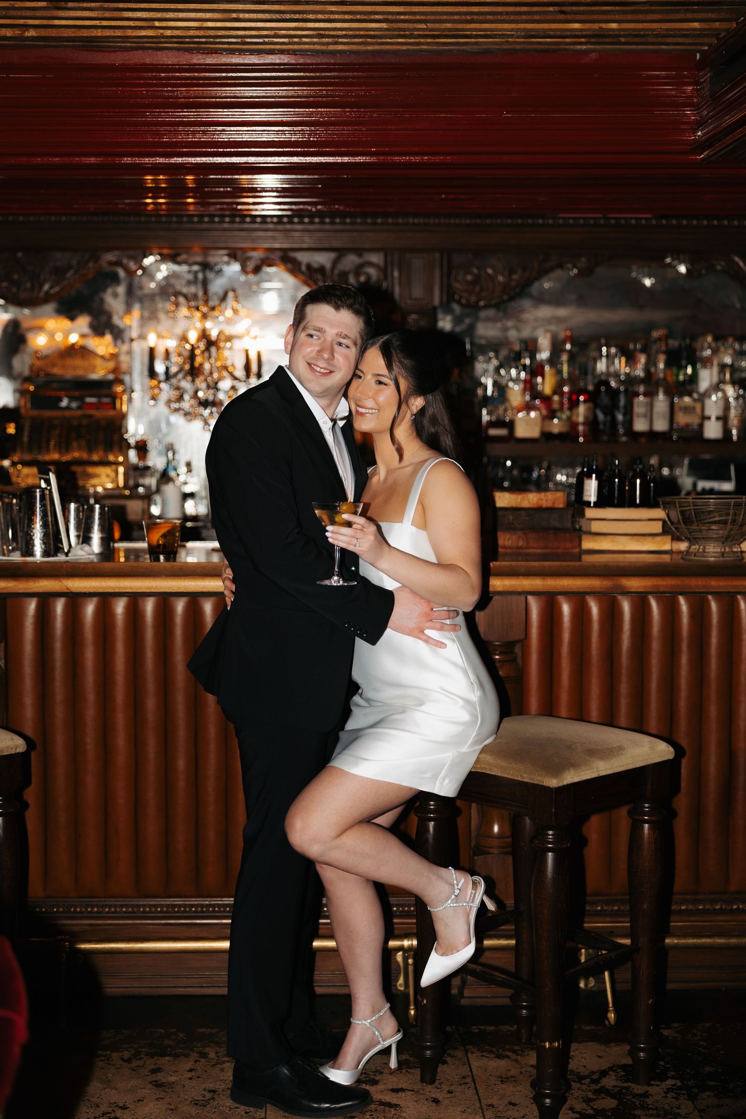 Newlyweds share playful moment at bar counter during wedding reception.